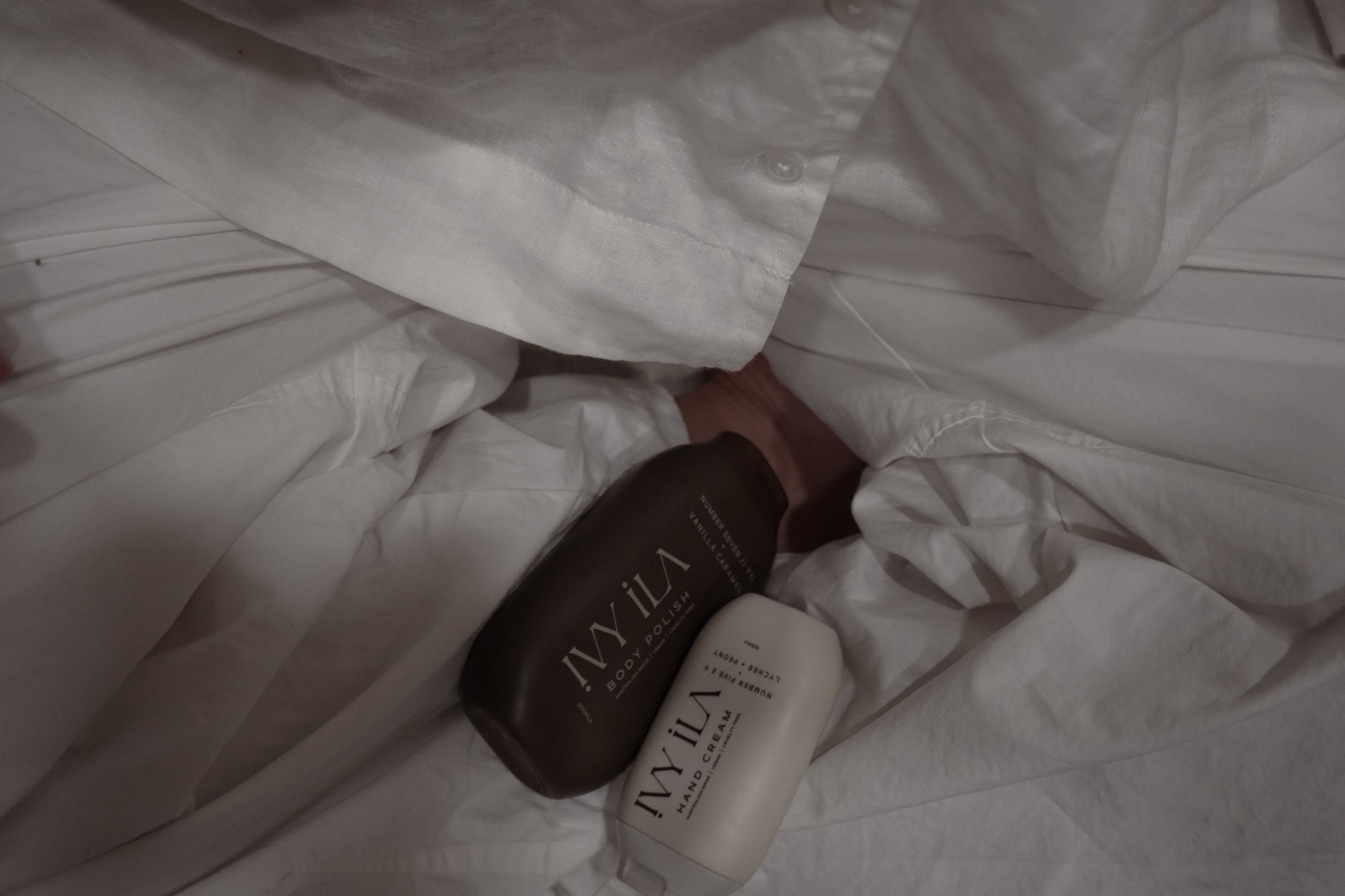A collection of skincare and body care products including a bottle of hand cream, a small white container, and two bottles labeled 'Lily' with black and white labels, nestled among white tissue paper.