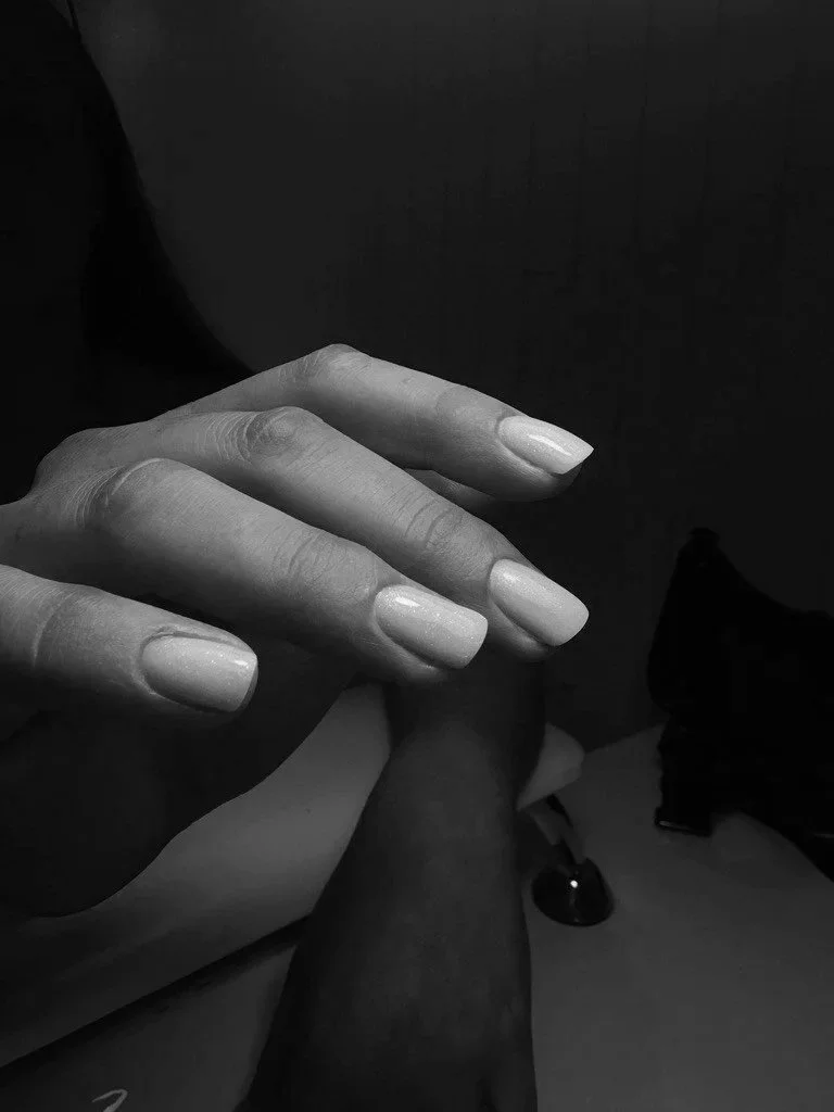 A close-up black and white photo of a hand with well-manicured nails, gently resting on another person's leg.