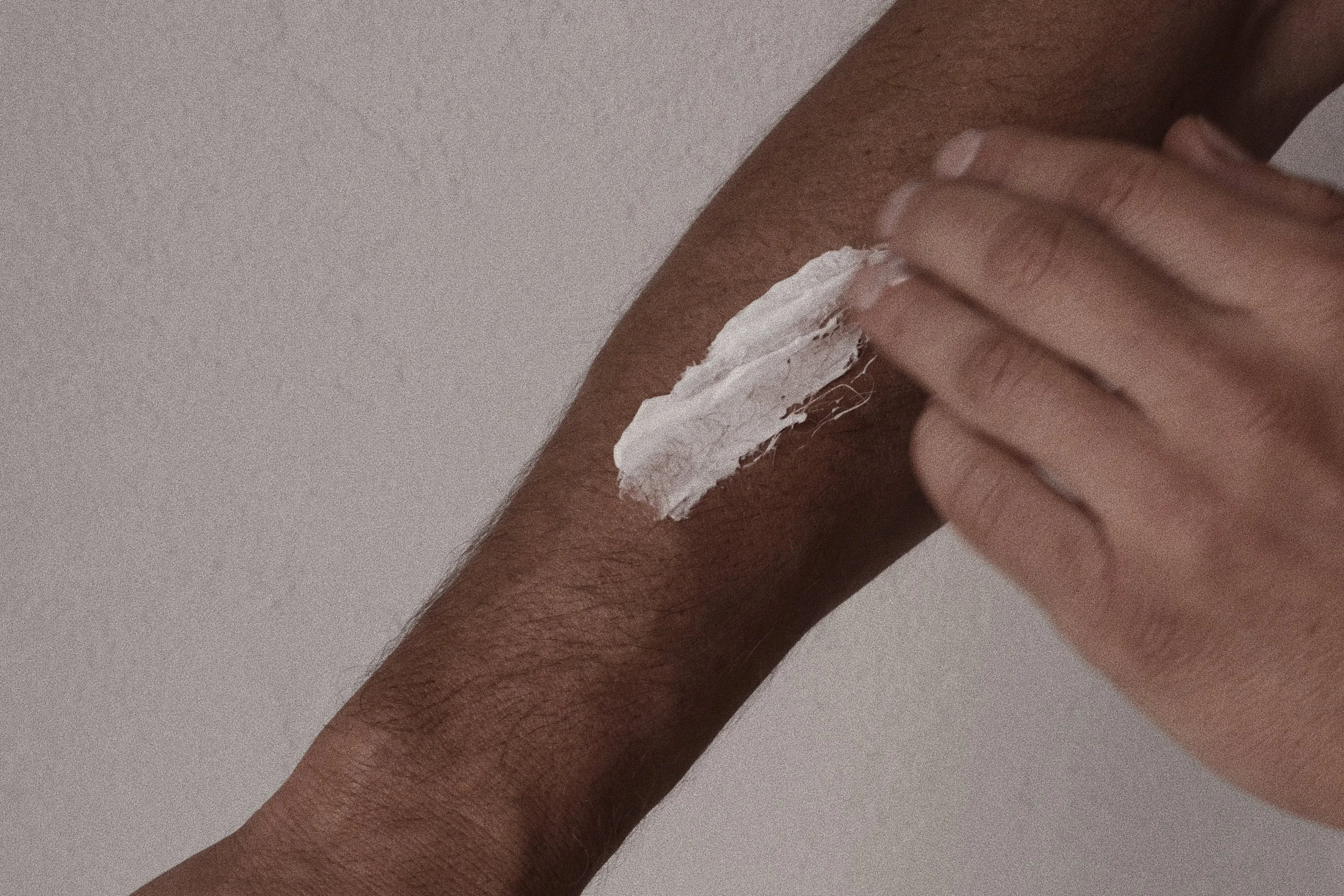 A person applying white cream on their skin with their fingers.