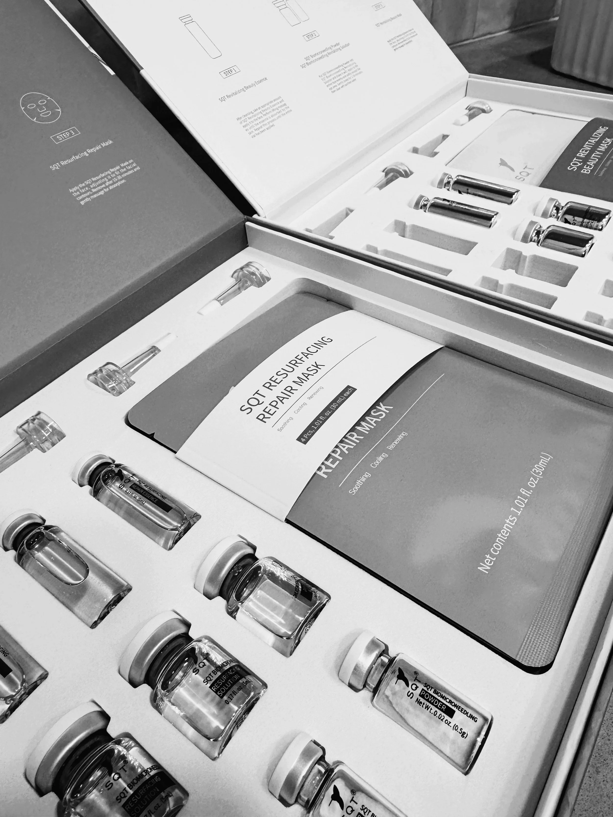 Open box containing multiple small test tubes with liquid, a box labeled "SQT Resurfacing Repair Mask," and instruction booklet for skincare products.