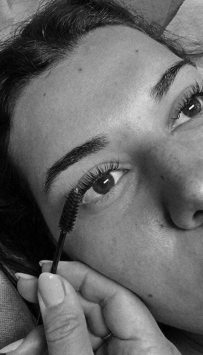 Close-up of a woman applying mascara to her eyelashes, with focus on her eye and eyebrow.