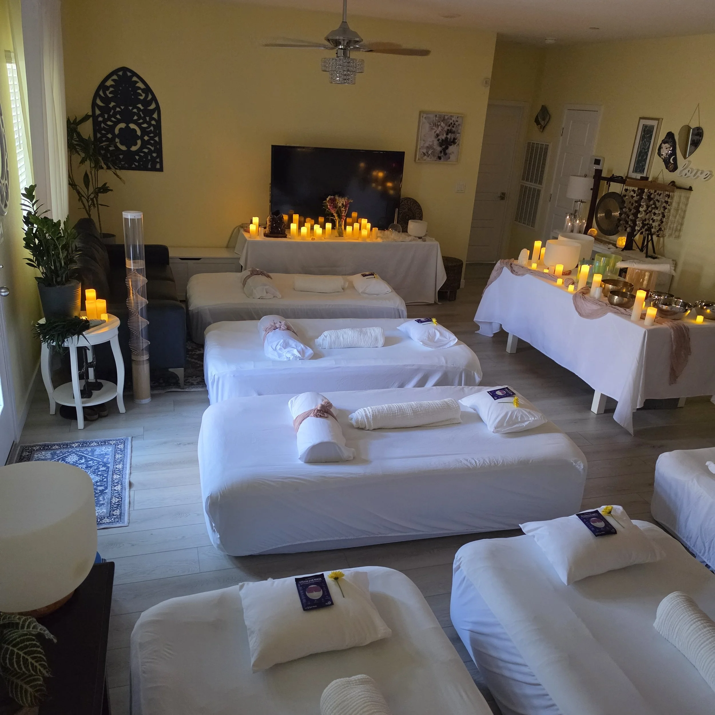 Elevated immersive sound bath space prepared with crystal singing bowls, candlelight, and cushioned beds designed to support relaxation, nervous system restoration, and intentional rest.