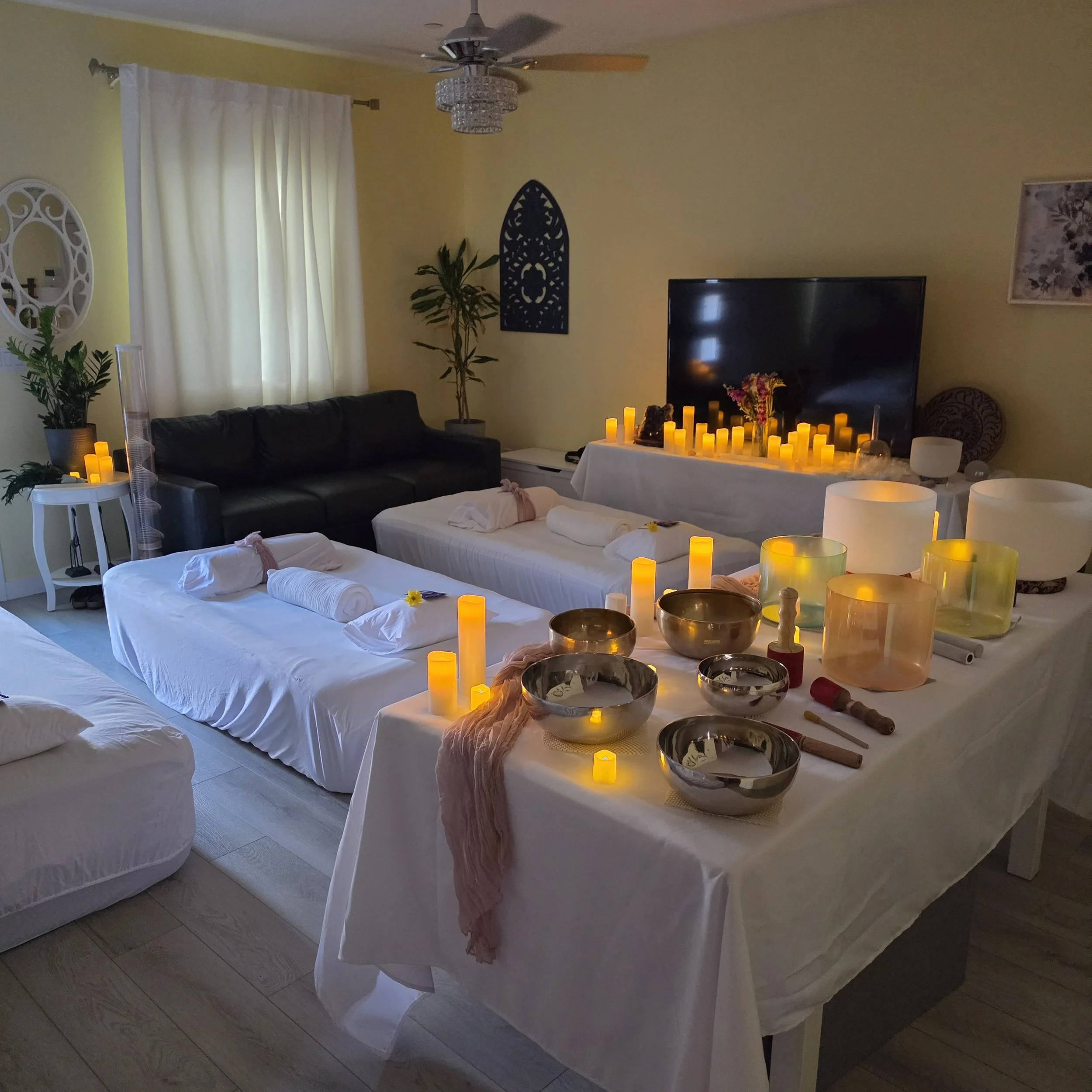 Elevated immersive sound bath space prepared with crystal singing bowls, candlelight, and cushioned beds designed to support relaxation, nervous system restoration, and intentional rest.