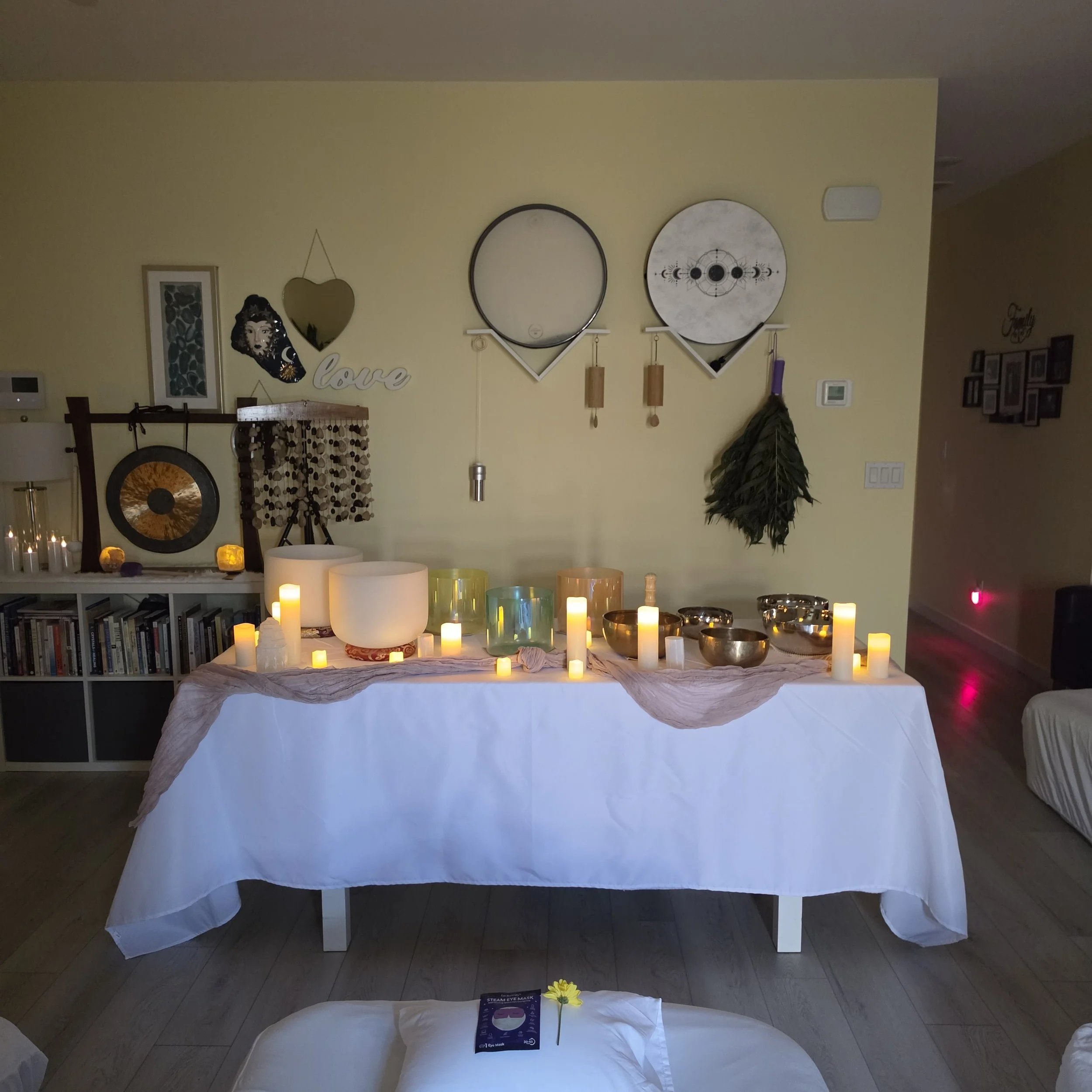 Candlelit sound healing altar featuring crystal singing bowls, metal bowls, crystals, and immersive wellness instruments arranged to support relaxation, meditation, and nervous system restoration.