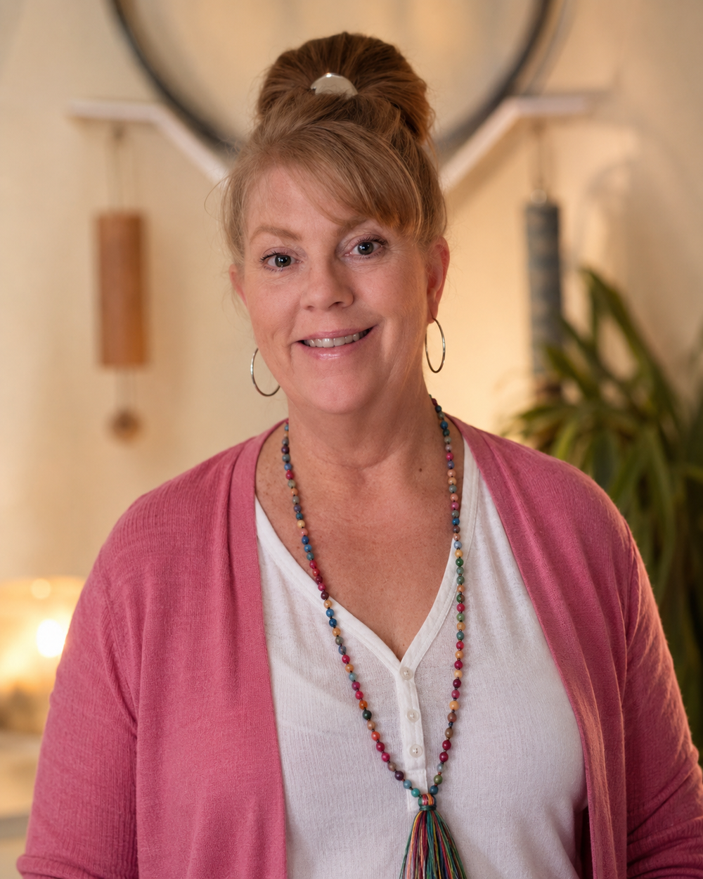 Portrait of Roberta Joseph of Selenite and Sound wearing a peach cardigan and crystal necklace in a warm indoor setting.