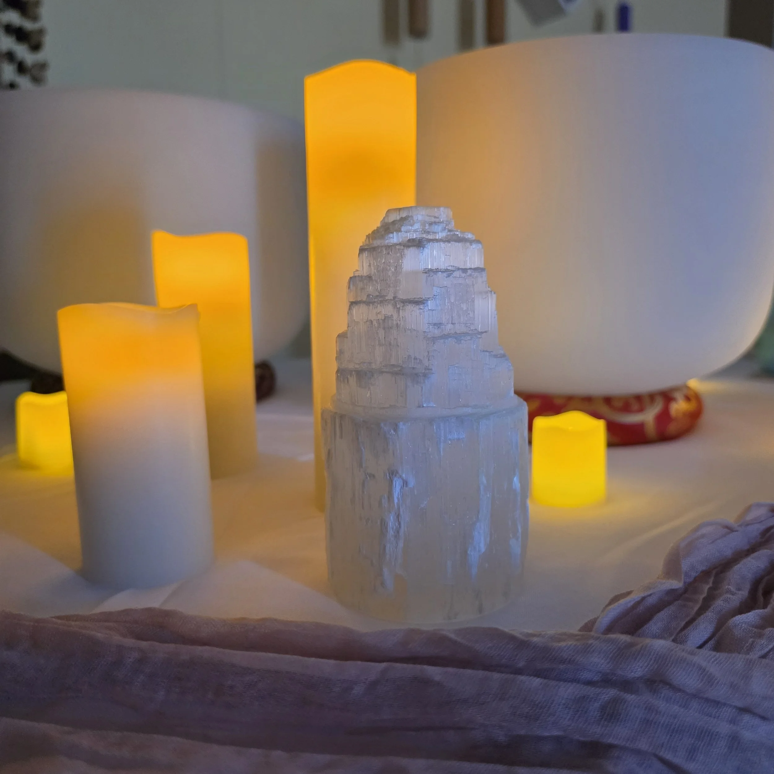 Close-up of selenite crystal towers surrounded by candlelight and crystal singing bowls in a calming sound healing environment designed to support relaxation, clarity, and nervous system restoration.