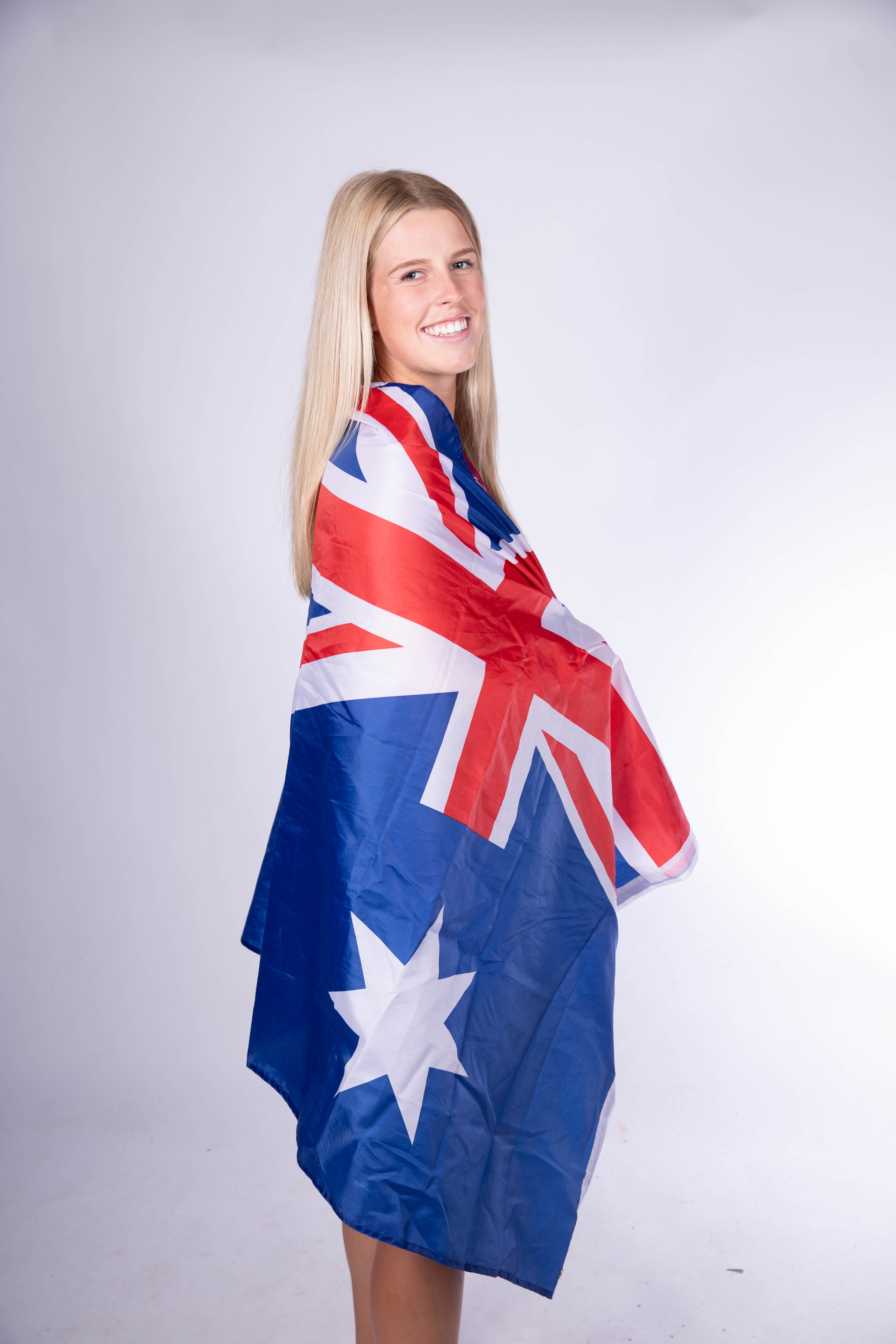 A smiling blonde woman with long hair wrapped in an Australian flag, standing against a plain white background.