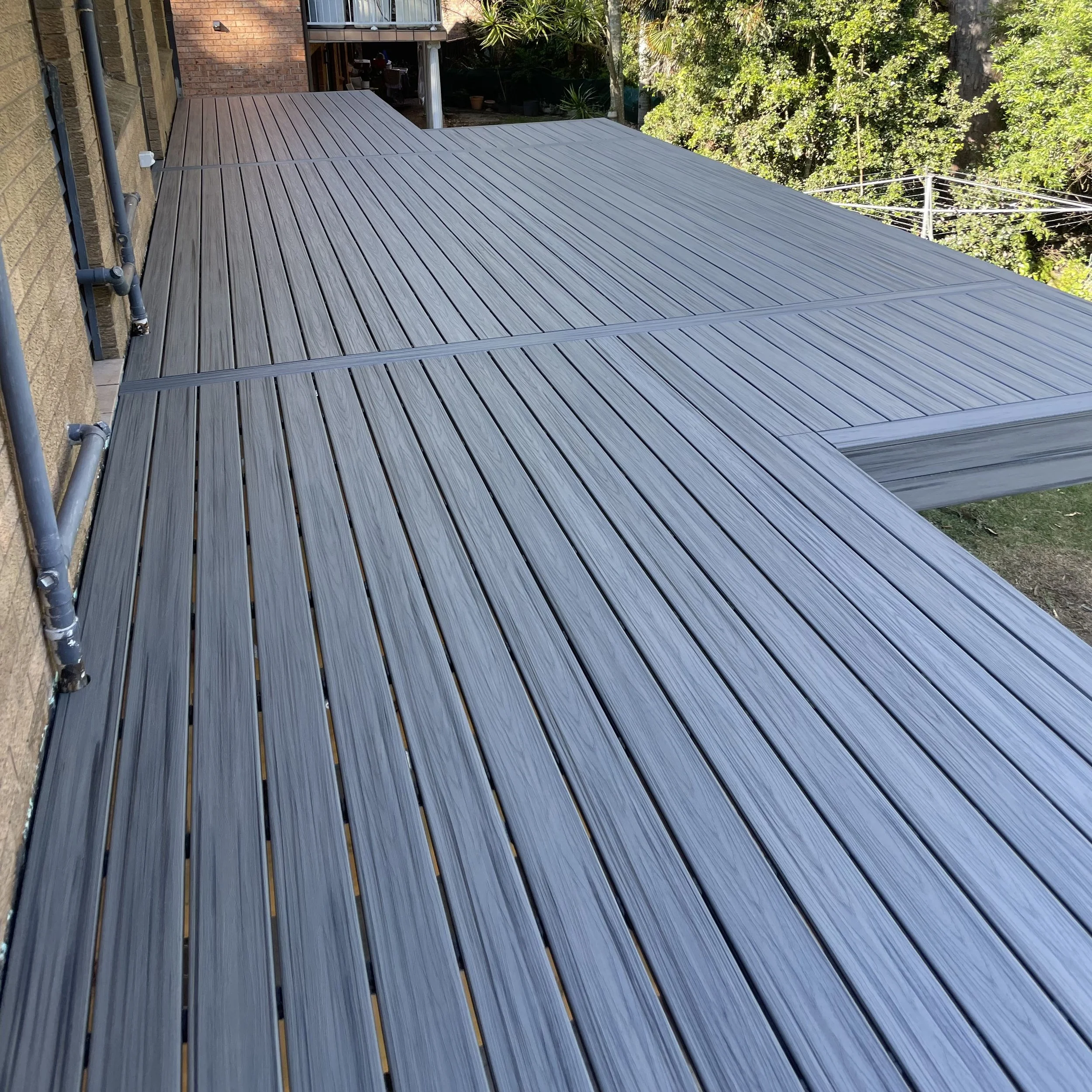 New composite deck attached to a house with brick and stone exterior. The eco friendly and low maintenance deck is surrounded by trees and other greenery.