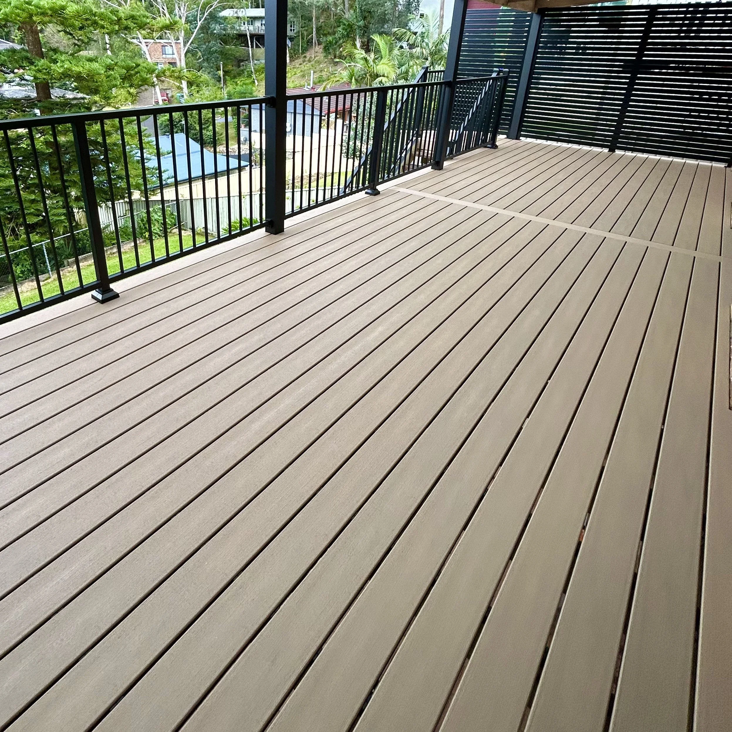 A balcony with beige composite planks, black metal custom railing, and a privacy screen made of black horizontal slats. Built and designed by Platinum Decks. 