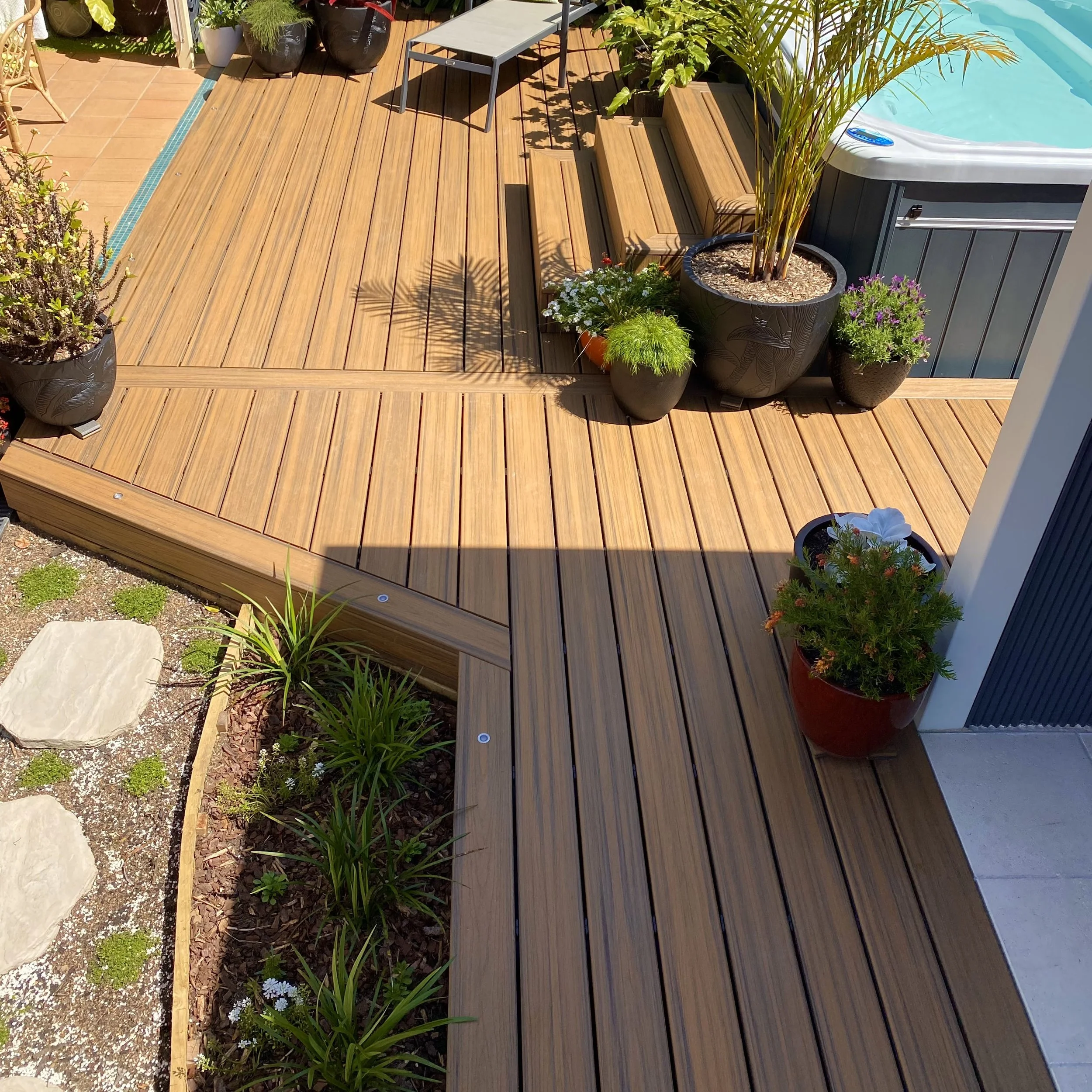 An extensive composite deck around a raised spa with relaxed seating and greenery, created by the Platinum Decks team