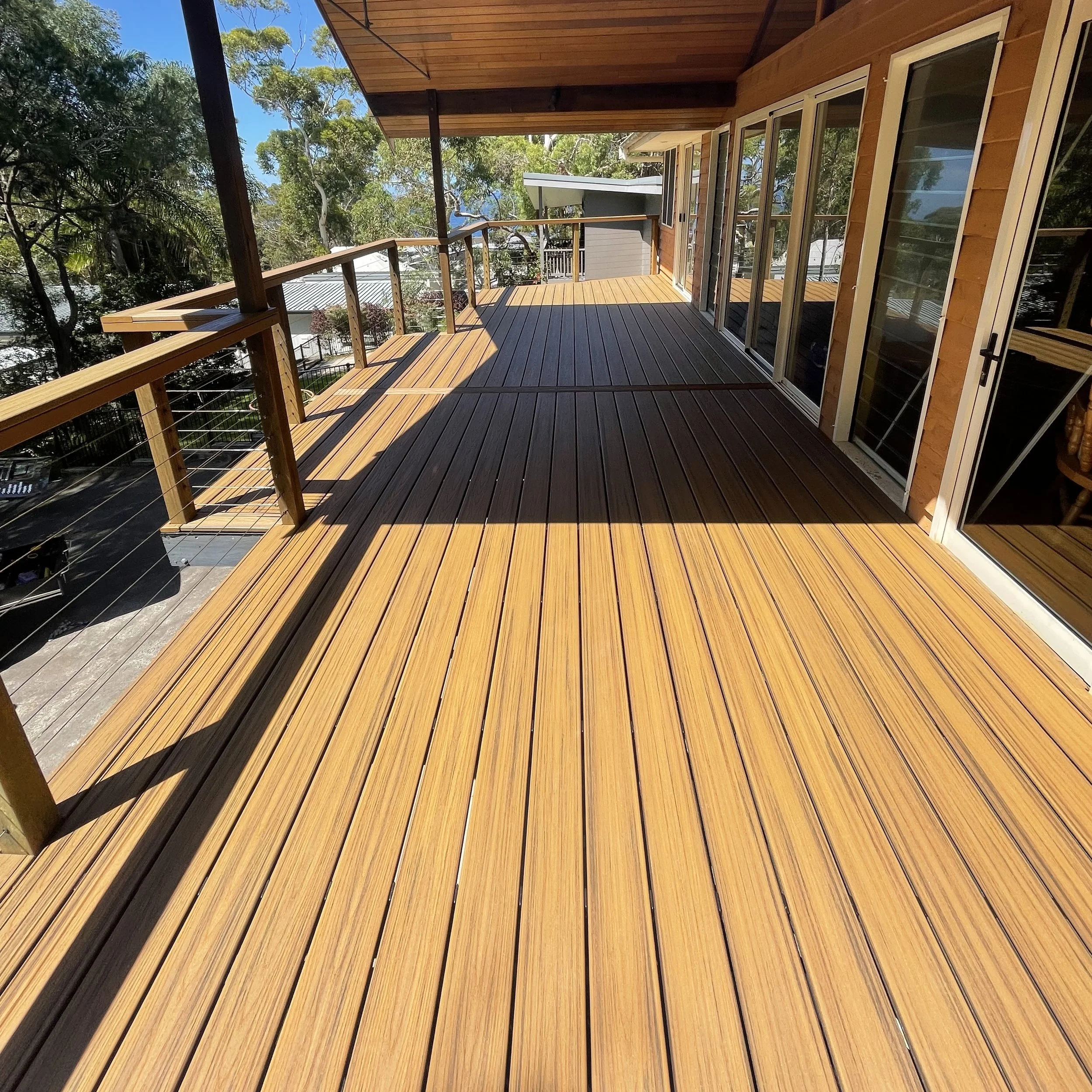 Stylish composite deck with complimentary balustrade railing, sliding glass doors, and a view of trees and rooftops in a residential neighbourhood on teh Central Coast.