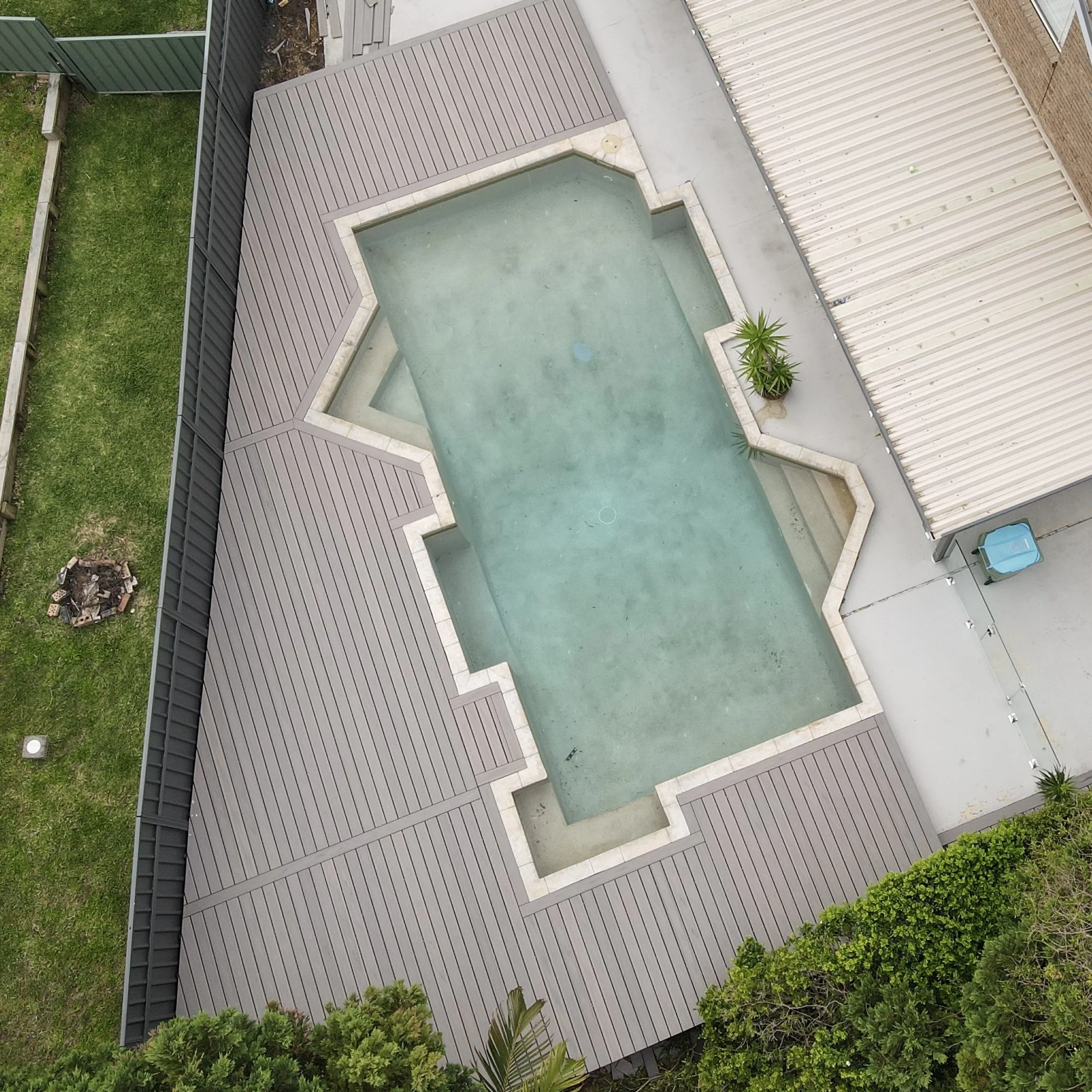 An ariel view of a light composite deck framing a geometric pool design with soft blue water, open lawn and clean edges, completed by Platinum Decks for a modern outdoor refresh
