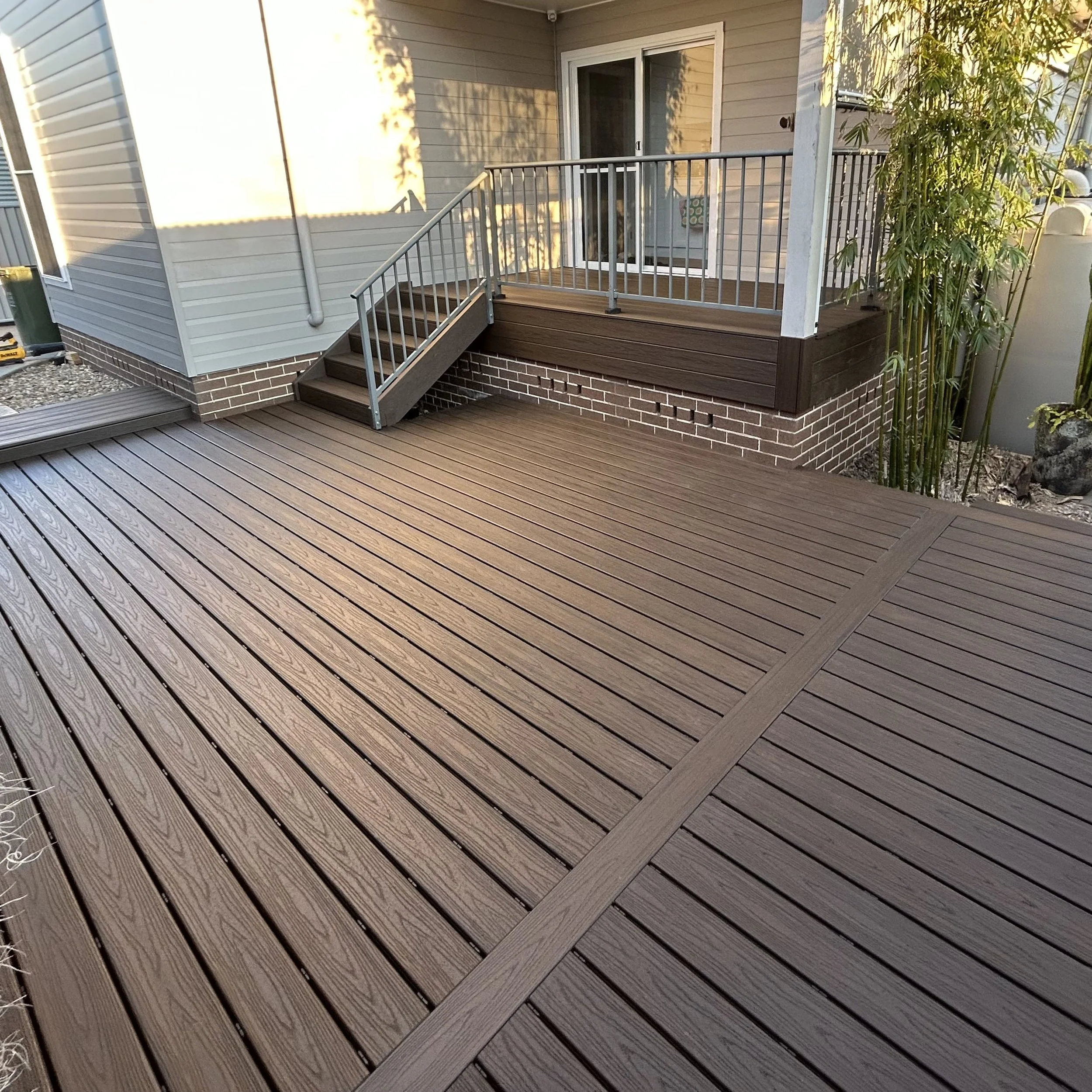 View of a backyard deck with modern composite decking with incorporated steps leading up to a sliding glass door. Built and designed by Platinum Decks on the Central Coast NSW.