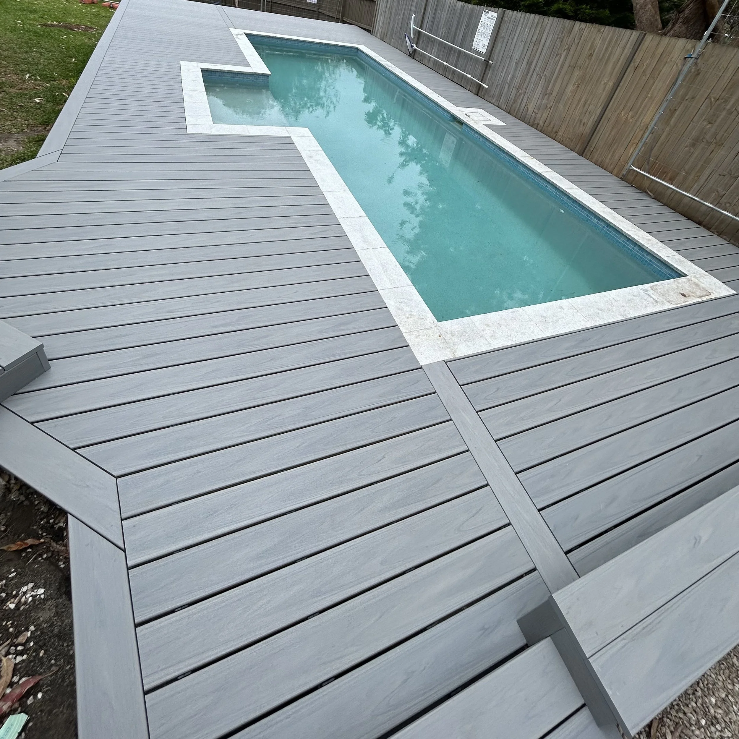 Swimming pool framed by Trex deck and tall timber fencing crafted by Platinum Decks to showcase minimalist, contemporary backyard design