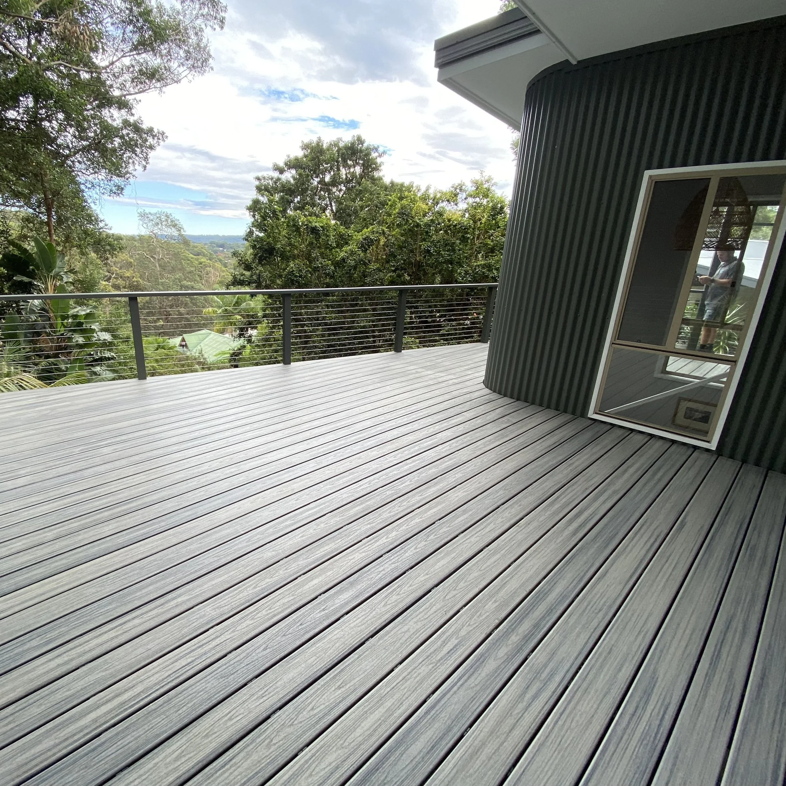 A large composite deck complete with black railing, and a modern Central Coast home with curved black siding. Built and installed byPlatinum Decks.