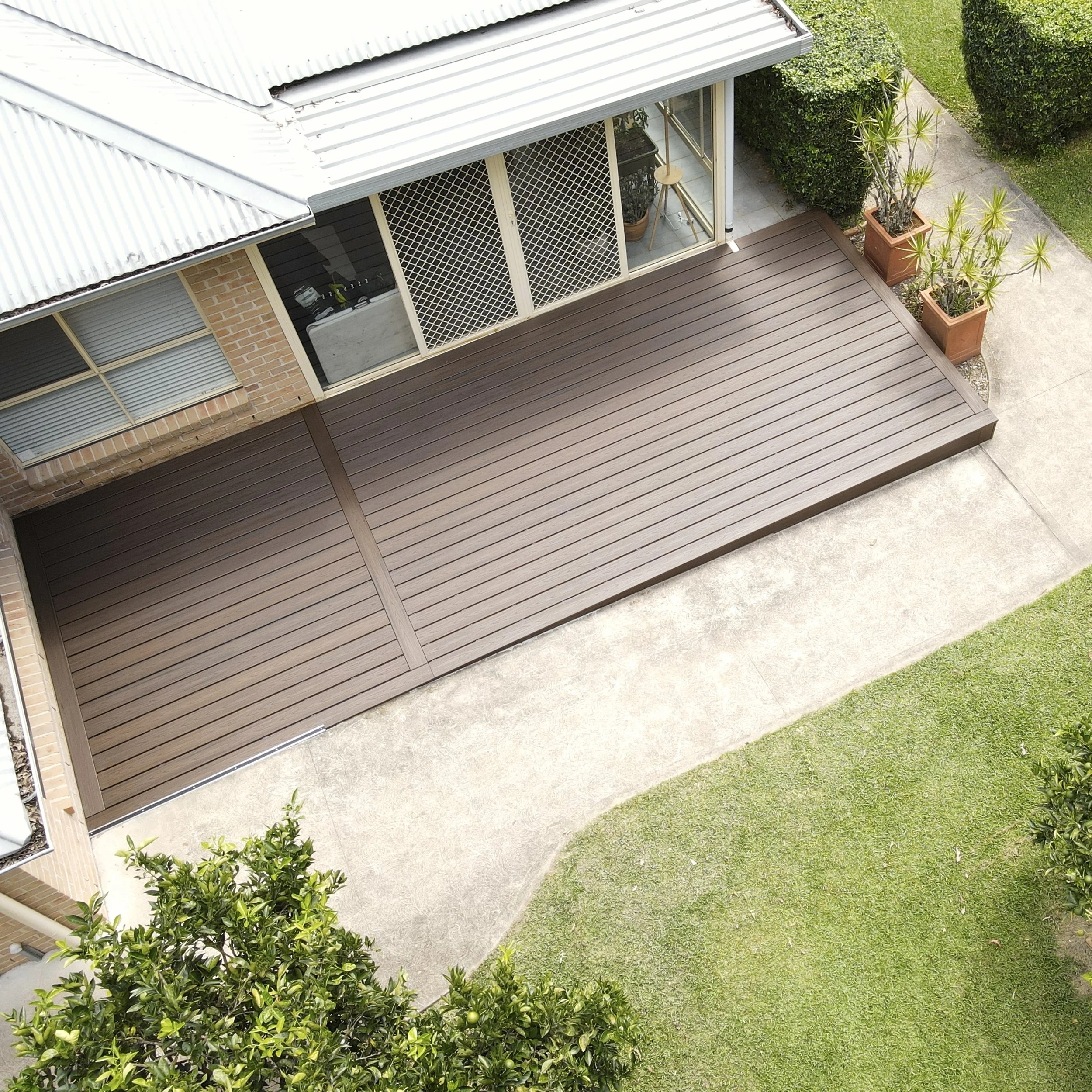 Trex deck in spiced rum, potted plants, and surrounding green lawn and bushes.