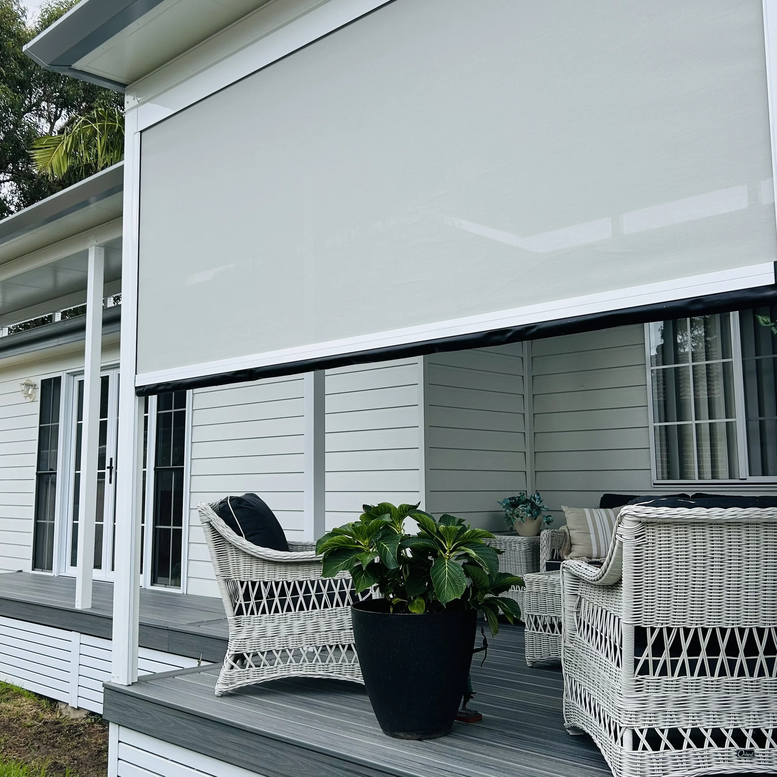 Outdoor entertaining area featuring white custom made privacy blind for a modern house with a custom patio roof build by Platinum Decks 