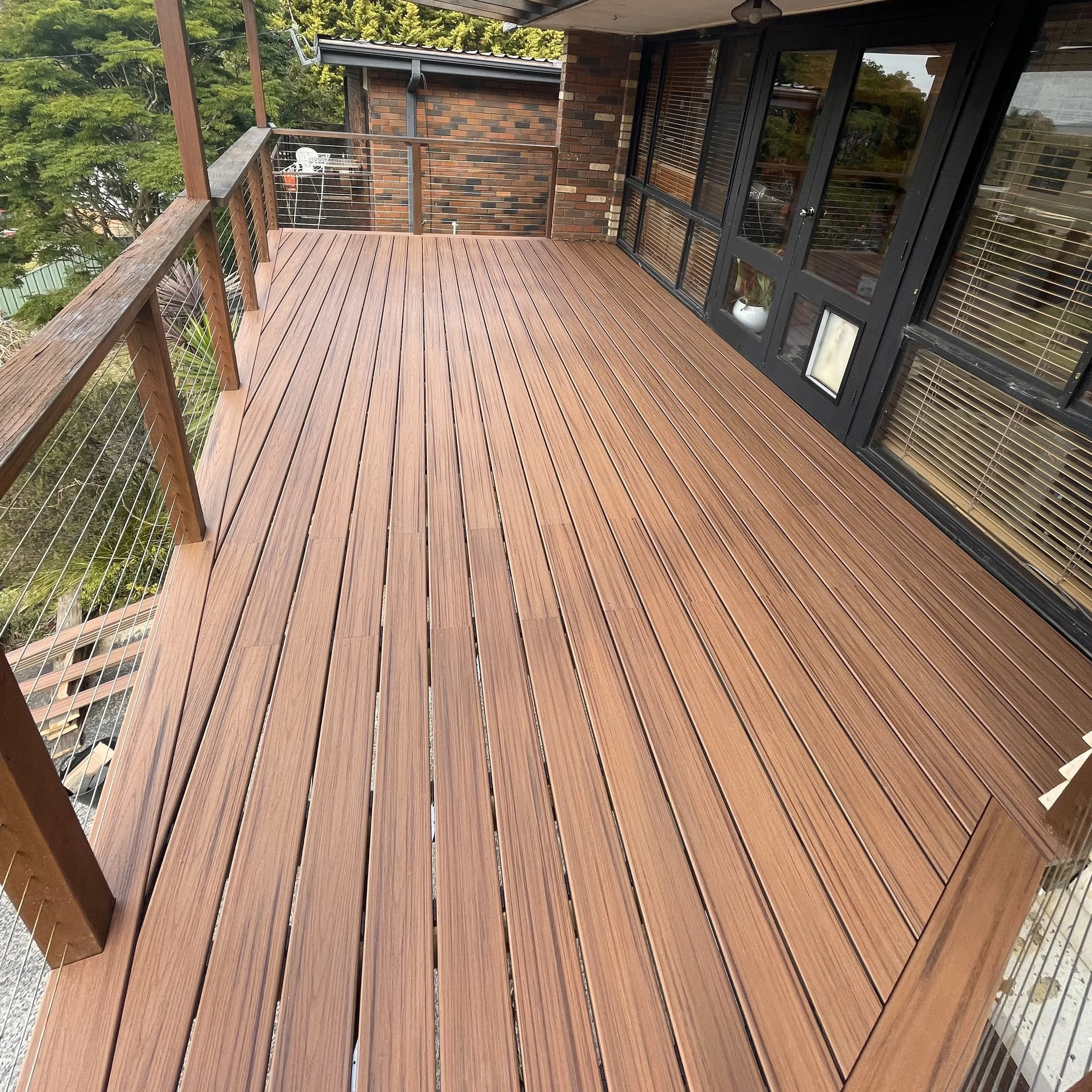 Elevated Trex deck in tiki torch with metal railing and leafy outlook completed by Platinum Decks to provide a luxury entertaining platform with modern architectural lines