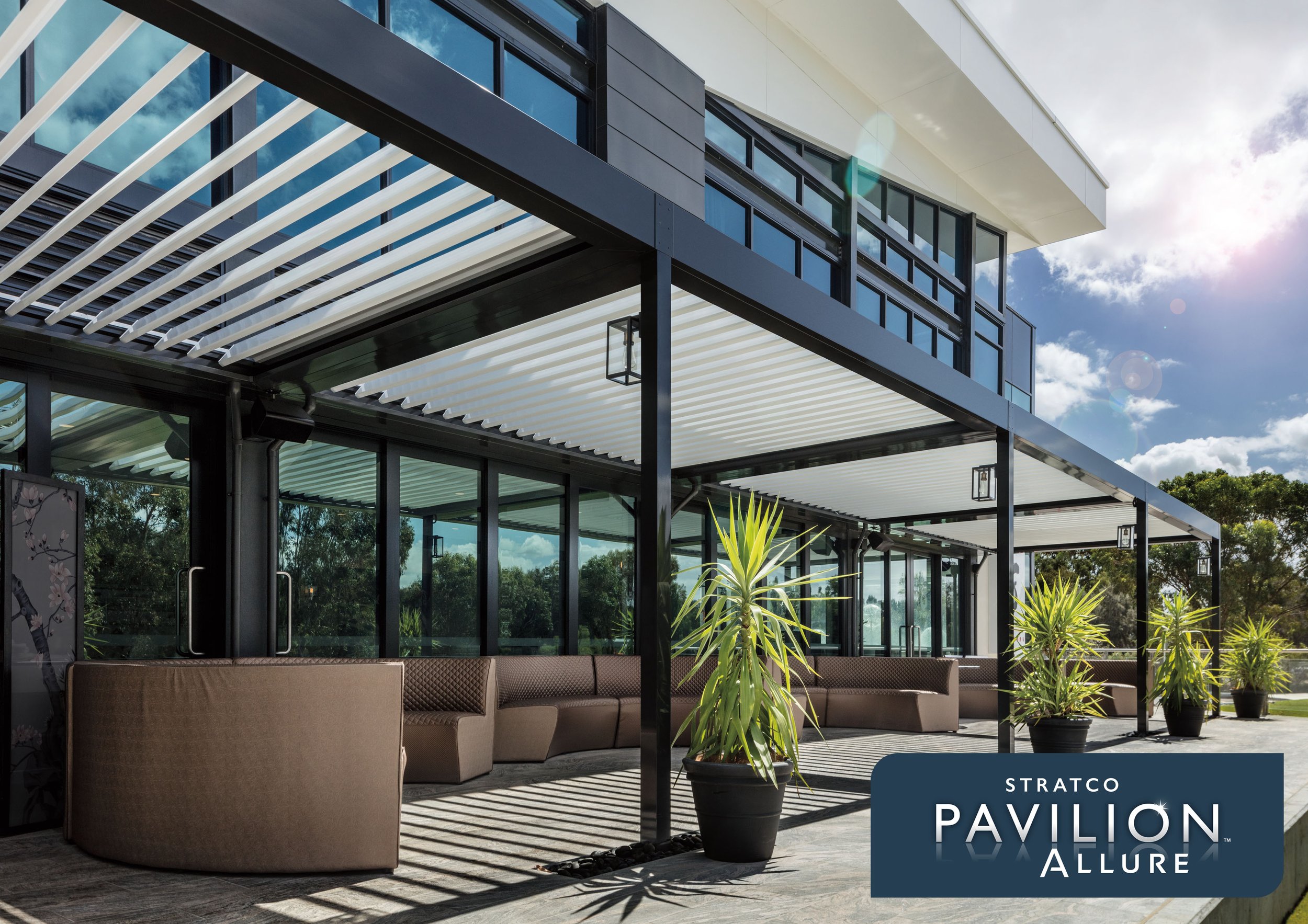 Modern building with glass windows, black and white exterior, outdoor seating area covered by a slatted pergola with white slats, potted plants, and a clear sky with the sun shining. Platinum Decks authorised installer.