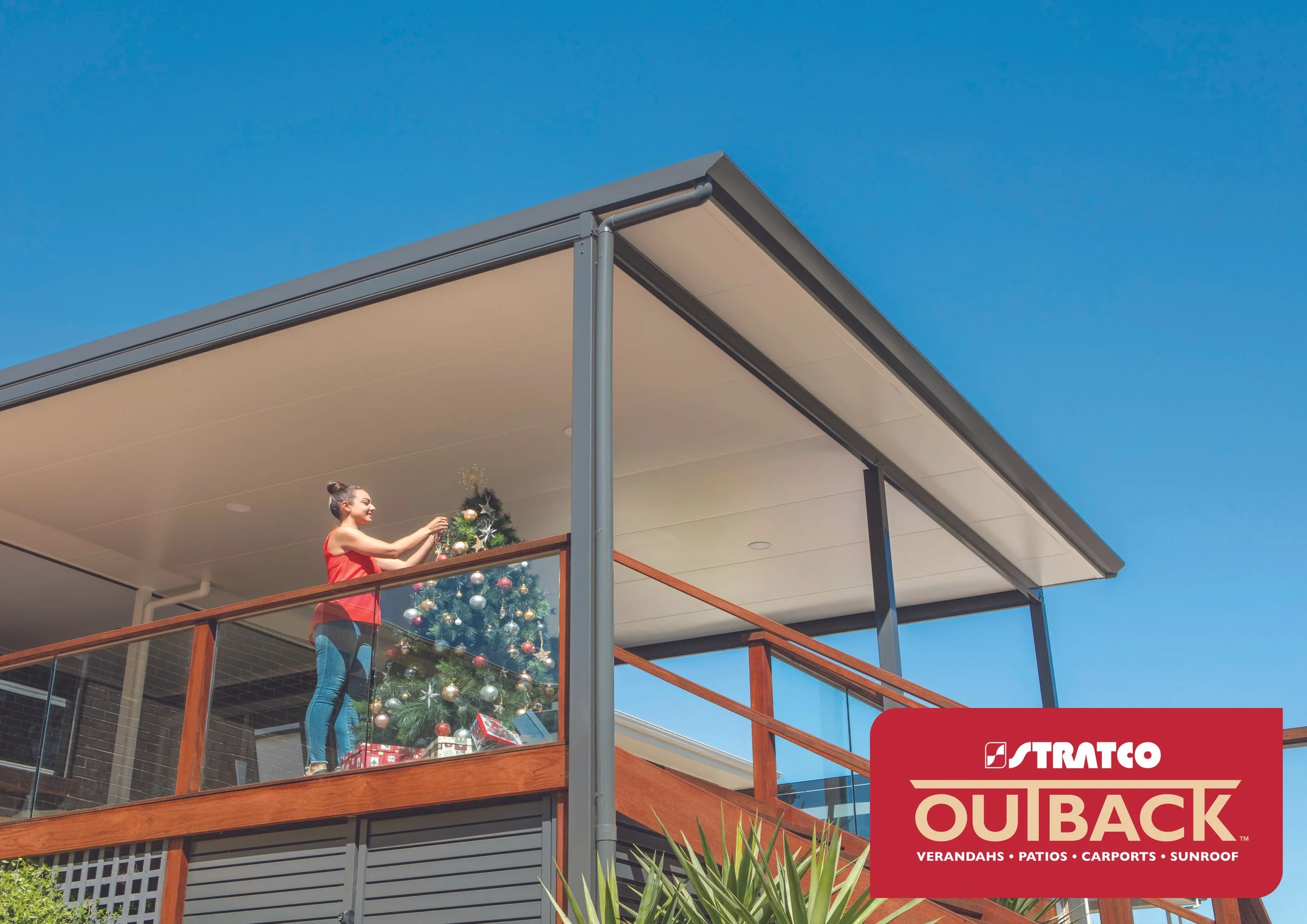 A woman decorating a Christmas tree on a balcony with a modern Stratco roof with a bright blue sky in the background. Platinum Decks authorised installer.