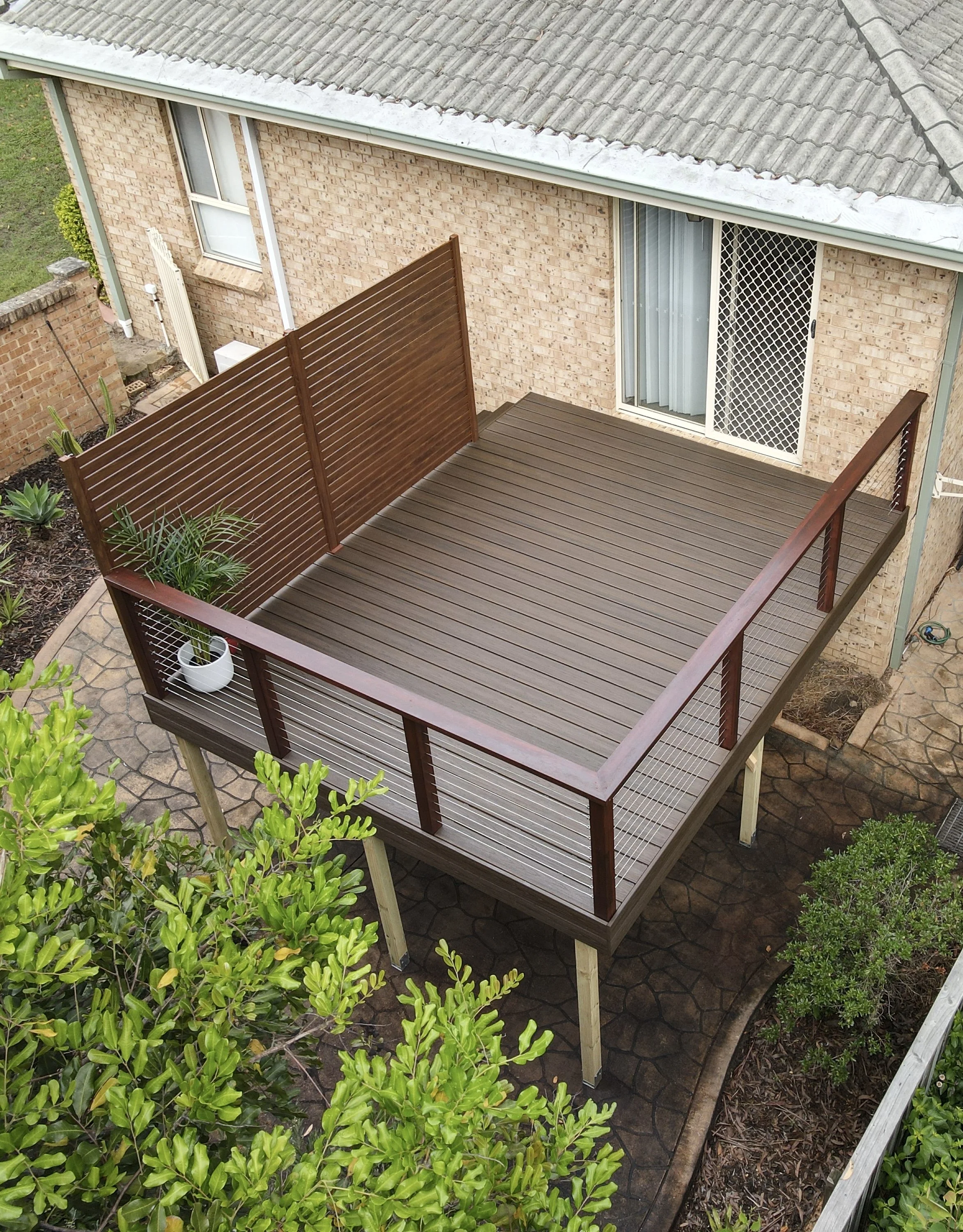 A backyard patio with a stylish composite deck complete with matching brown privacy screen and a lrage stair case down to the first storey. Built and installed by Platinum Decks. 