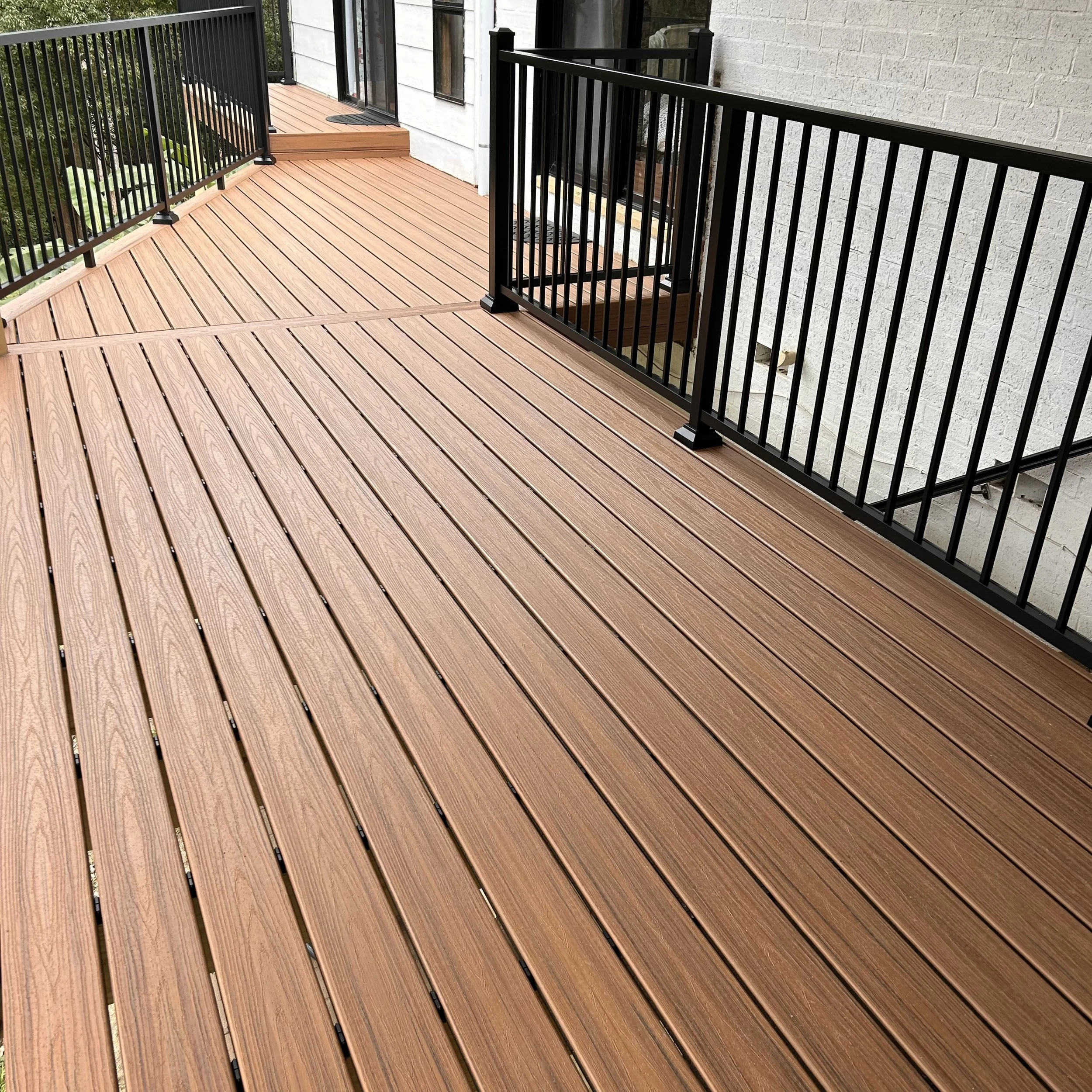 Fresh composite deck with black metal railing outside a white brick building, featuring sliding glass doors and a doormat. Built, designed and installed by the leading composite deck builder on the Central Coast.