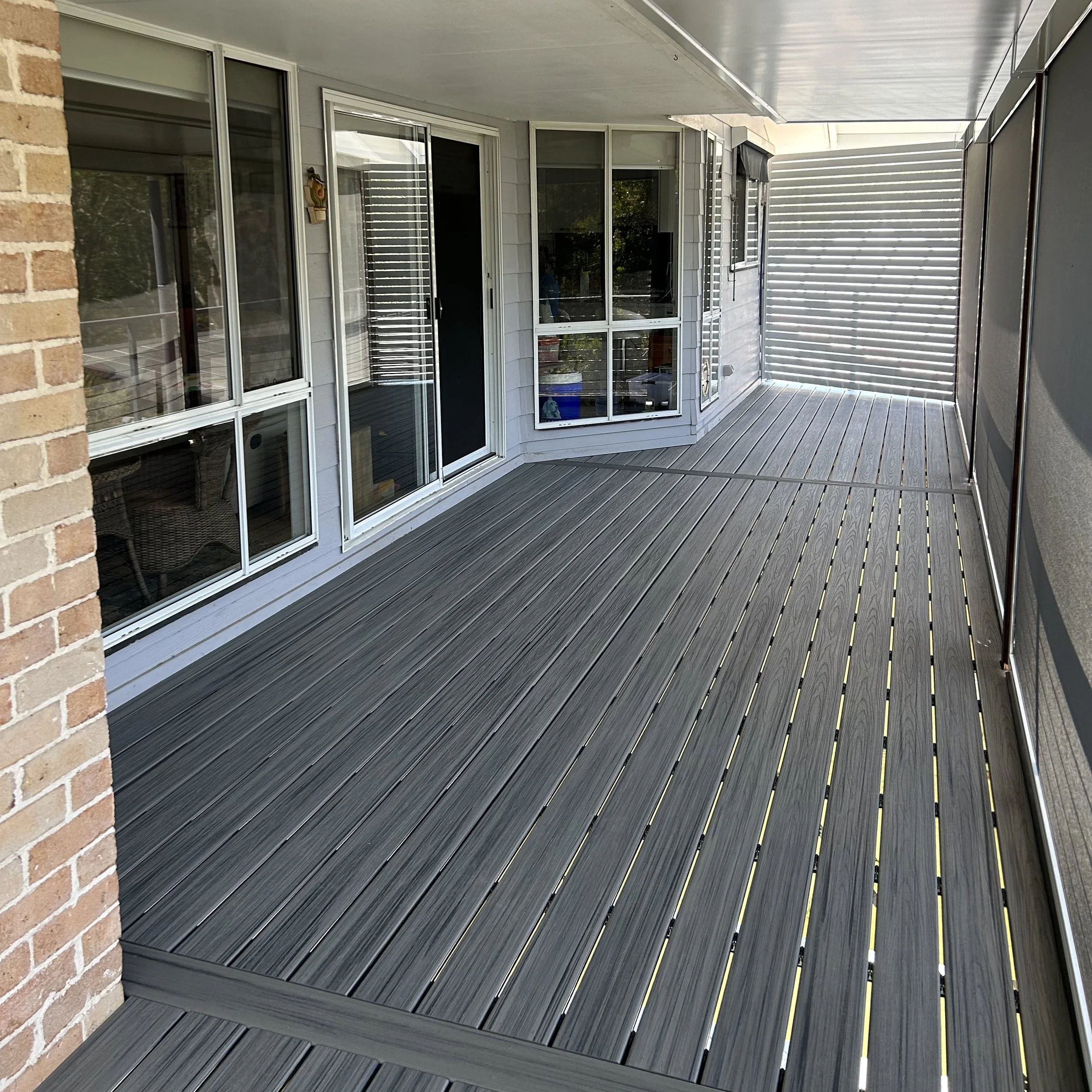 An outdoor residential composite deck alog the back of a Central Coast home, white siding walls, sliding glass doors, and a custom built privacy screen made of horizontal white slats on the right side.