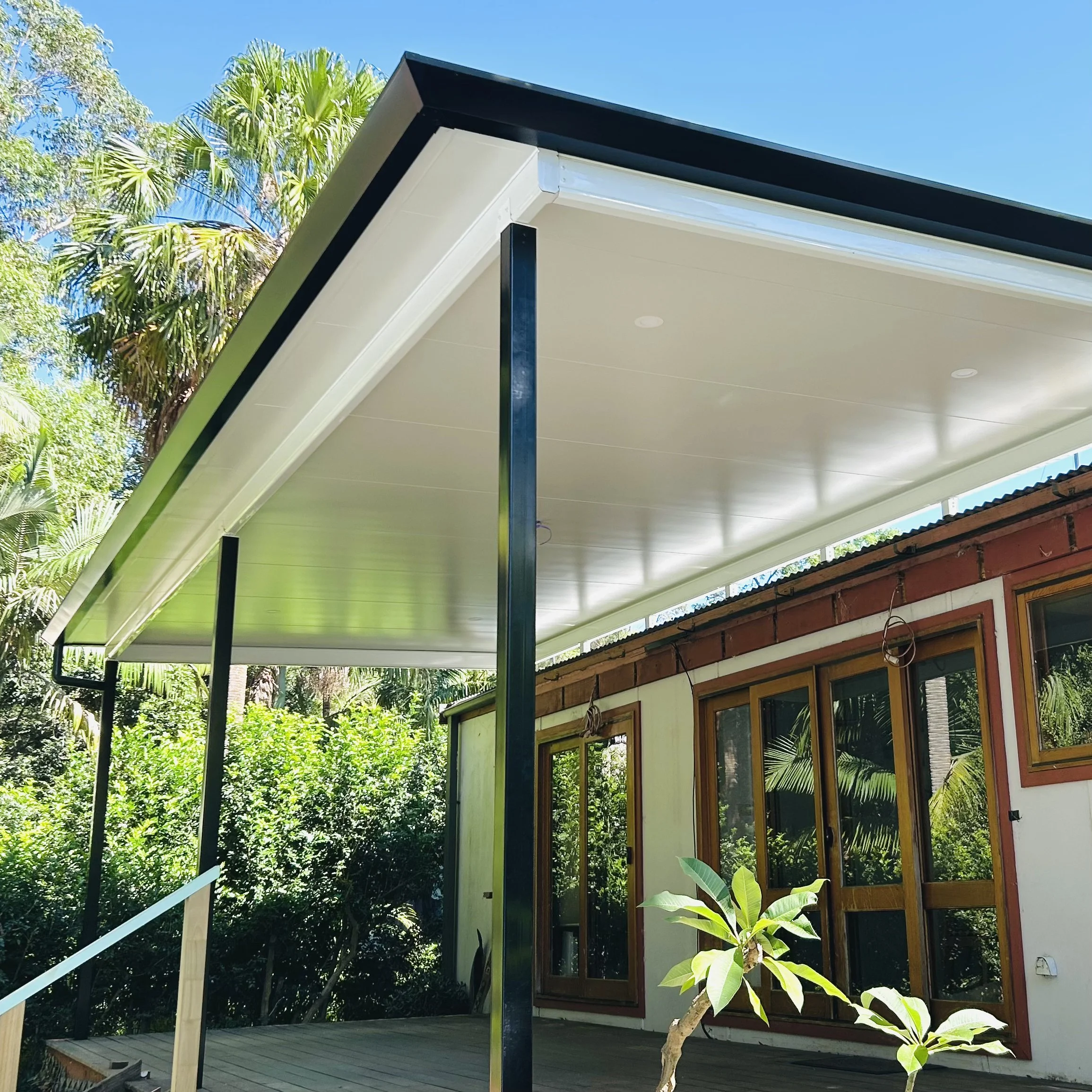 Stratco Cooldek patio framed by tropical greenery styled by Platinum Decks to blend luxury outdoor living with lush surroundings