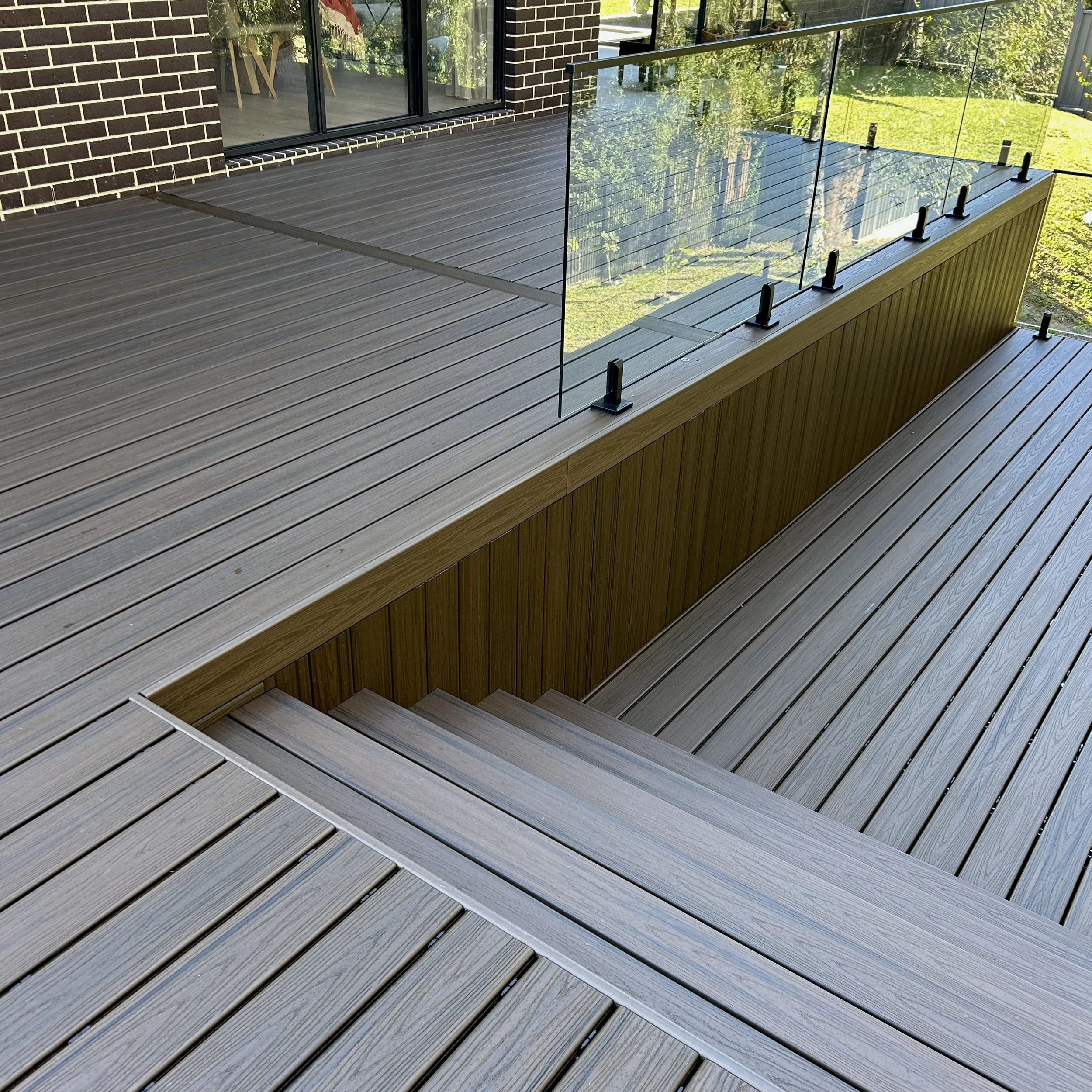 Trex deck in Spiced Rum with glass balustrade overlooking garden installed by Platinum Decks to deliver a refined, contemporary outdoor experience