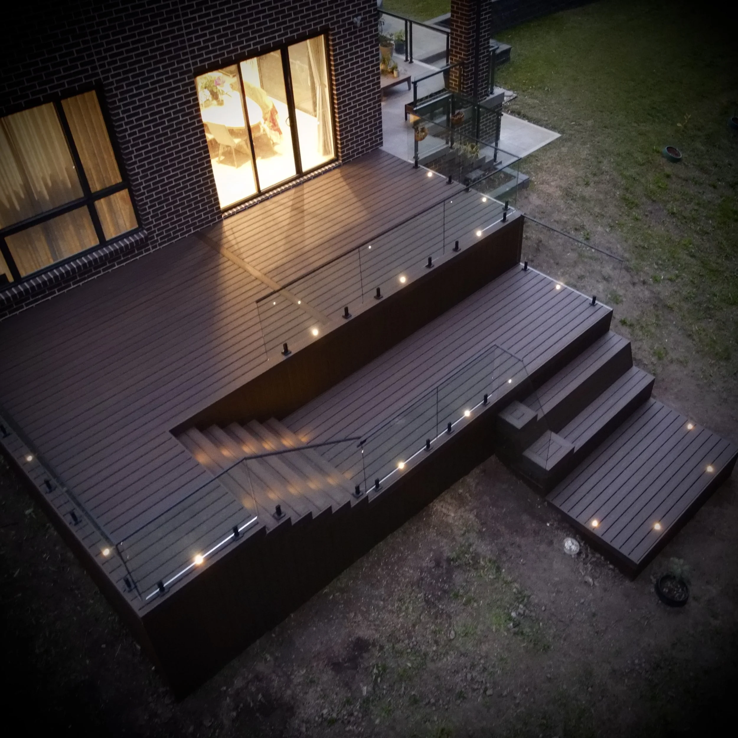 A nightime view of a Tiered Trex composite deck with integrated lighting and steps by Platinum Decks & Patios for modern entertaining
