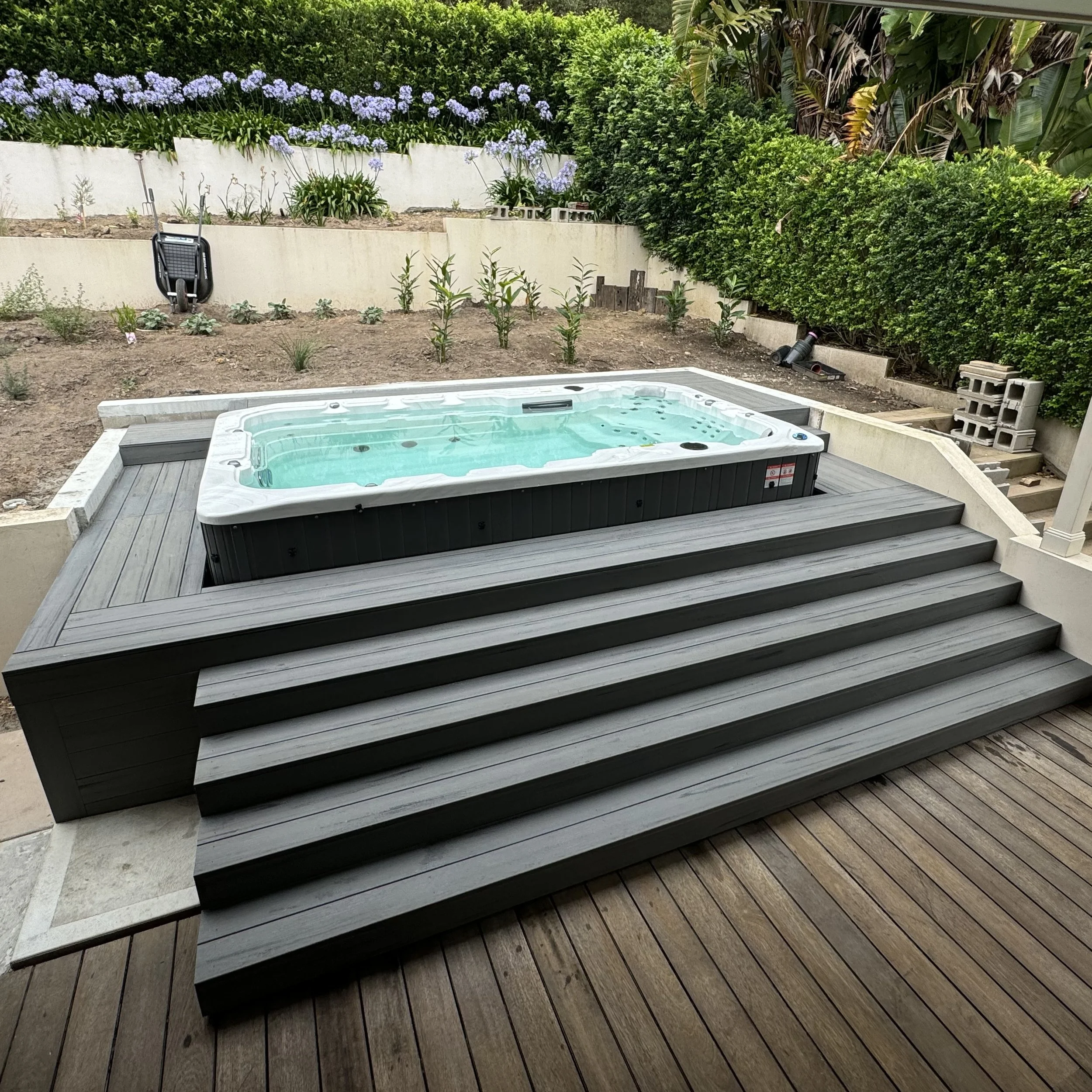 Composite deck with warm coastal tones surrounding a raised spa with steps and lush green landscaping, built by Platinum Decks on the Central Coast.