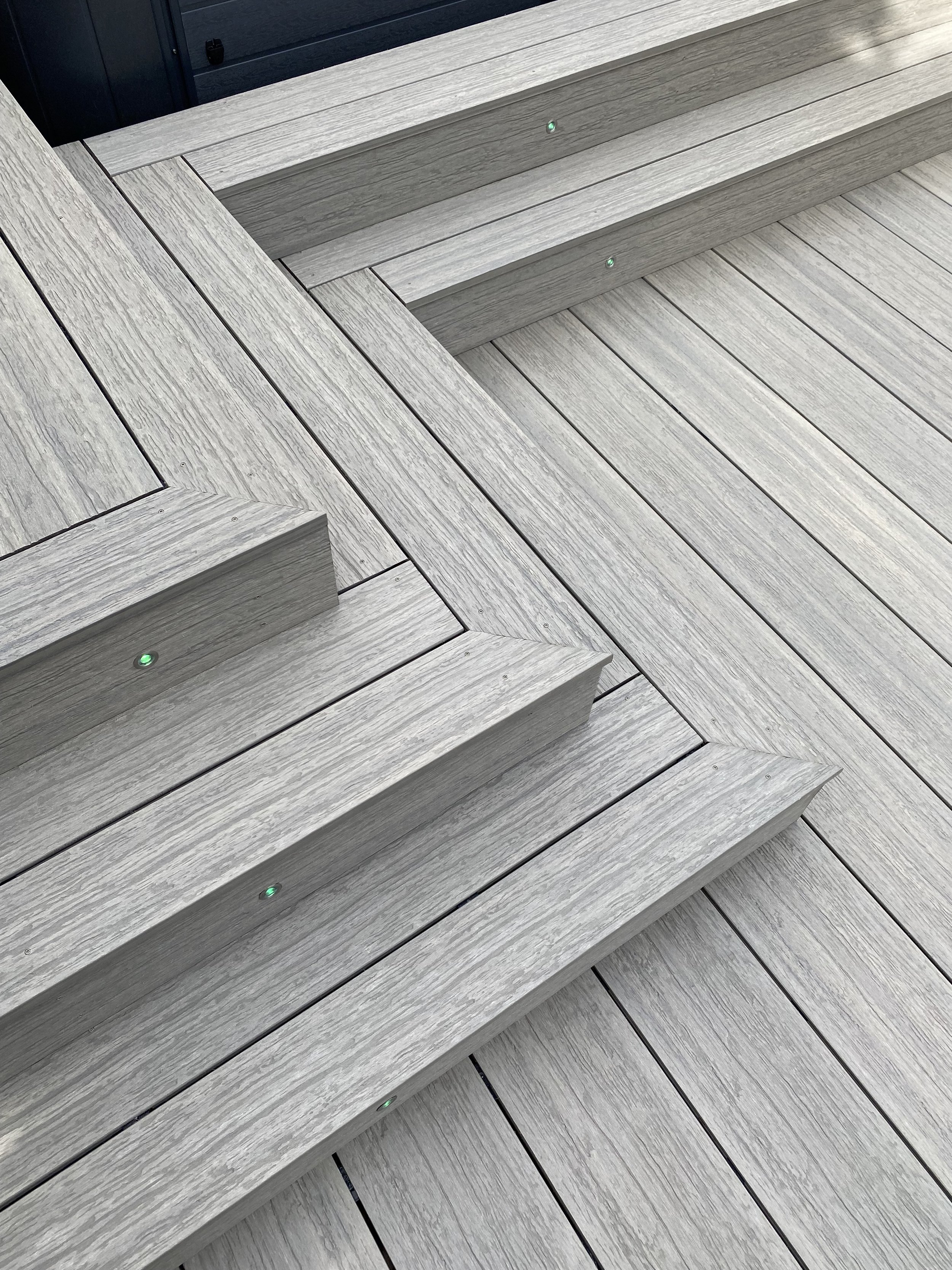 Close-up photo of a Trex Island Mist composite deck with steps, featuring small green lights embedded ideck, designed by Platinum Decks.