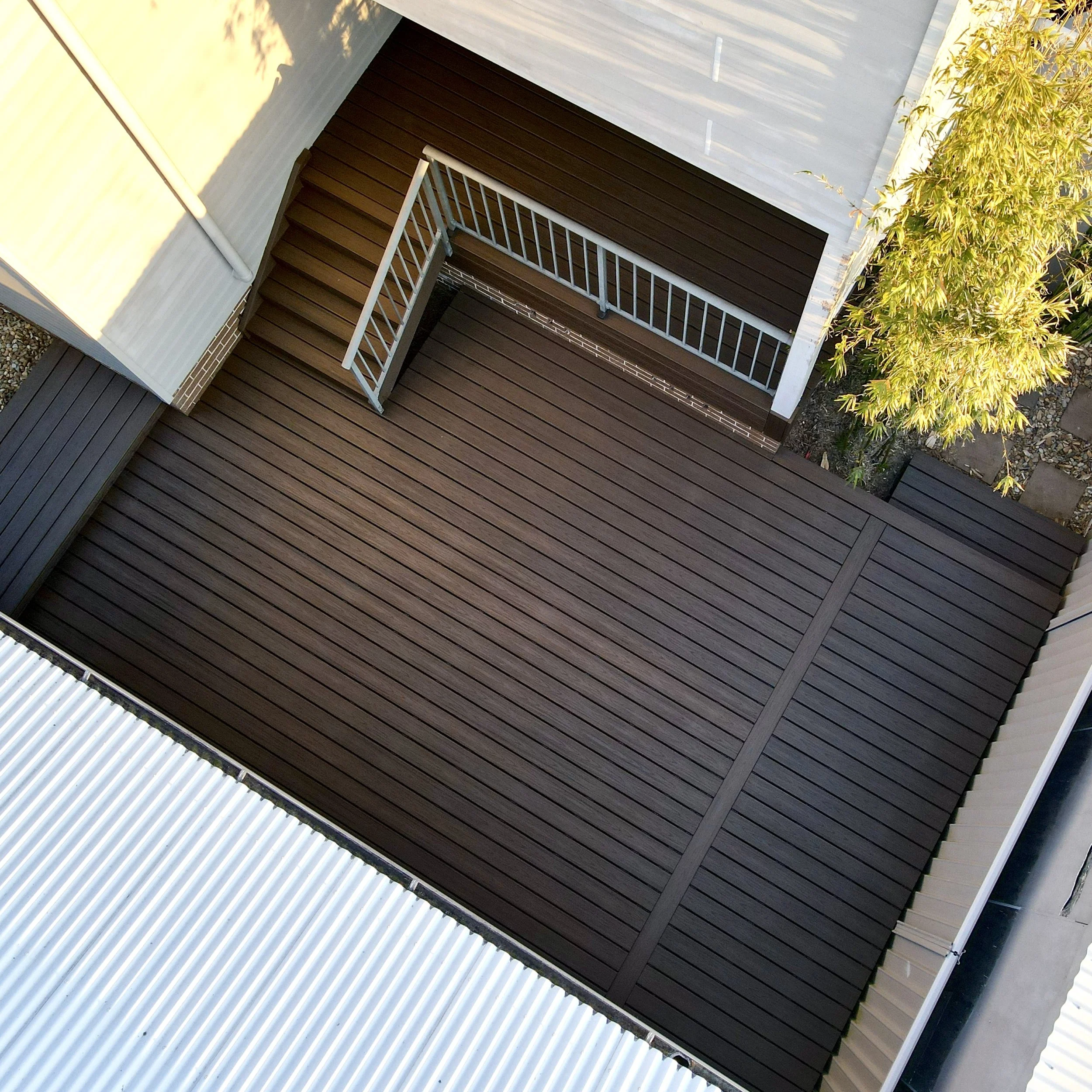 A modern outdoor composite staircase with brown wooden steps, white metal railing, and beige siding walls. All designed and built by Platinum Decks, Central Coast NSW