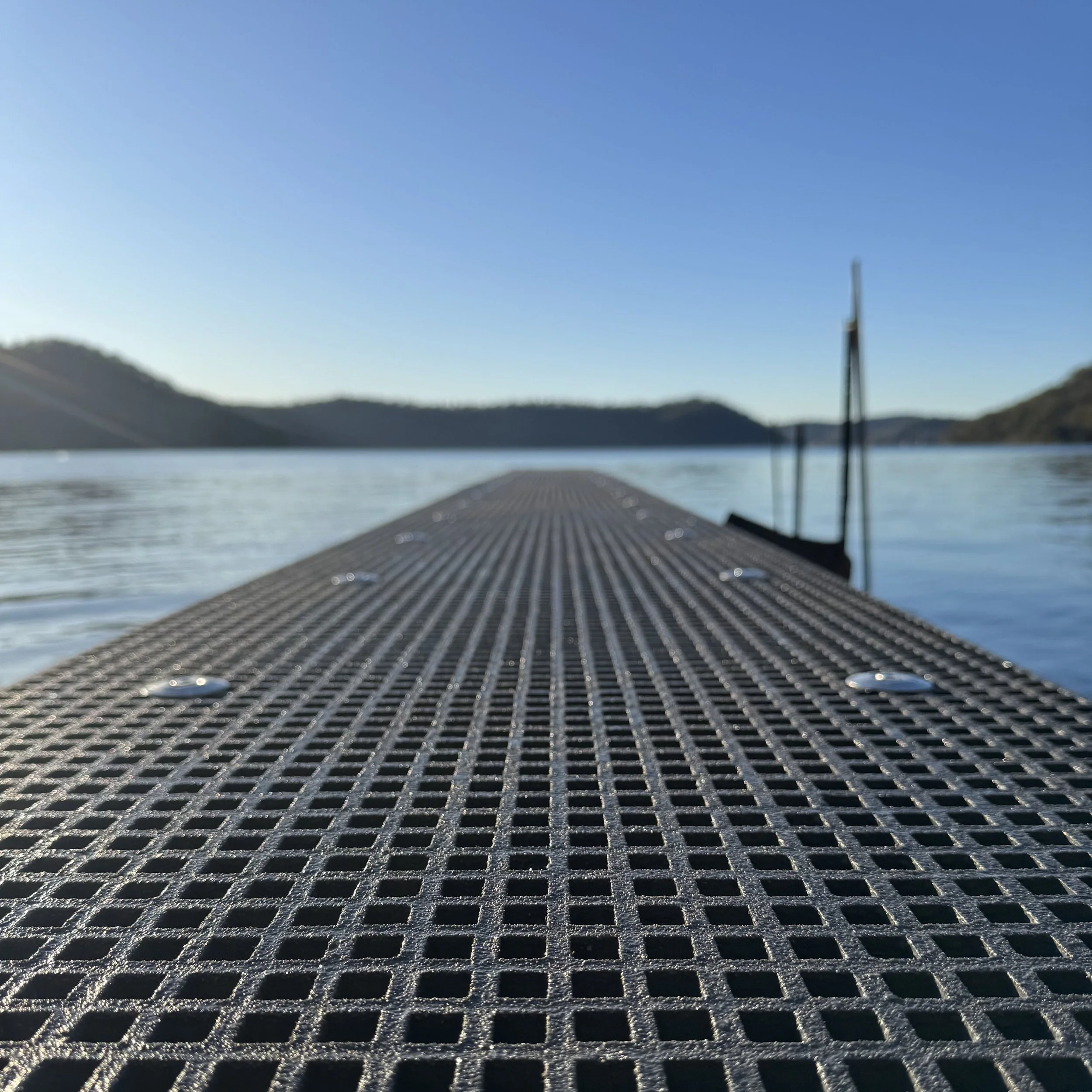 FRP dock platform over water with clear sky and rolling hills enhanced by Platinum Decks to showcase clean, modern waterfront structure