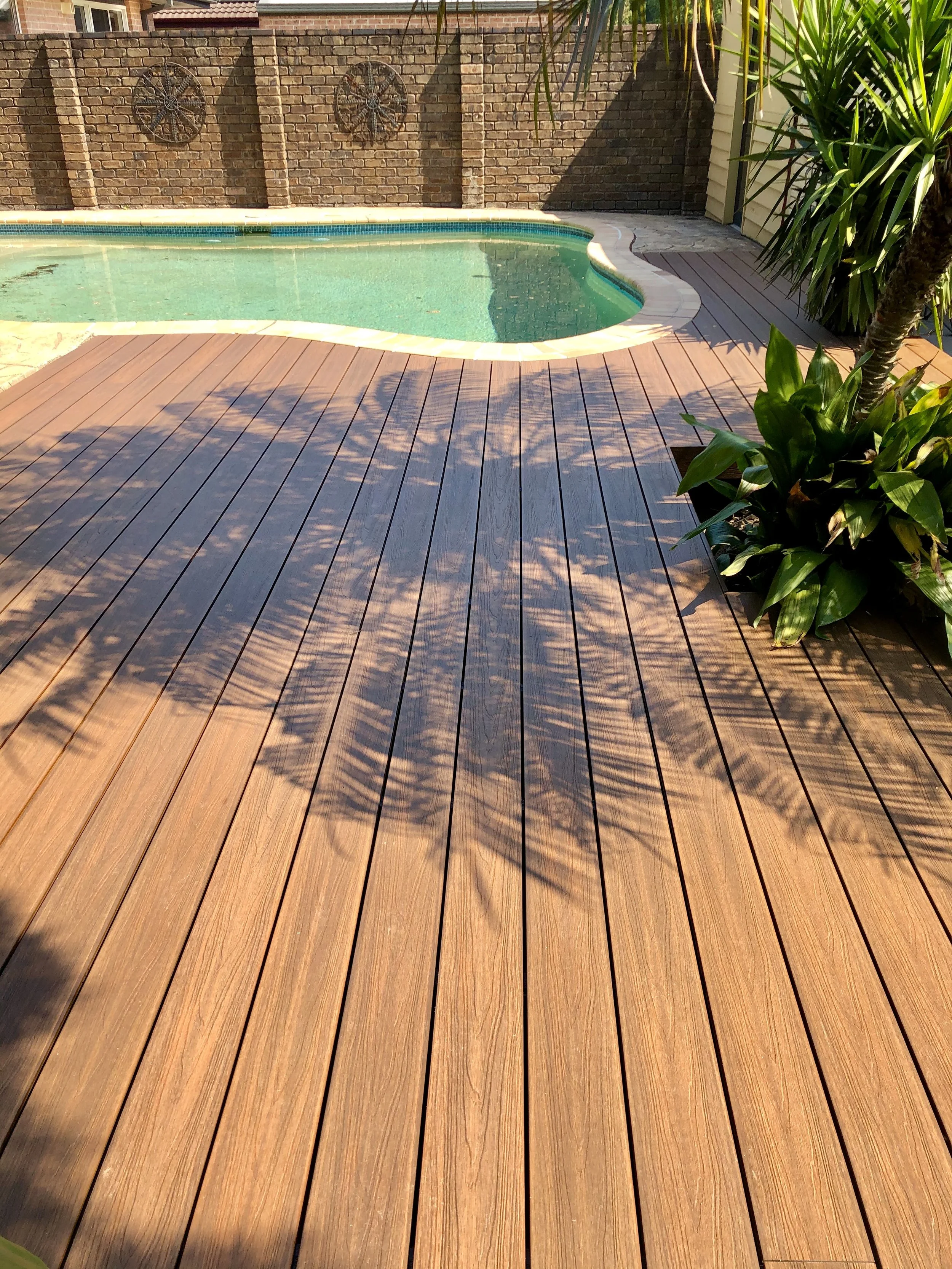 Swimming pool beside NewTechWood deck and decorative brick feature wall enhanced by Platinum Decks to blend natural textures with high‑end backyard design