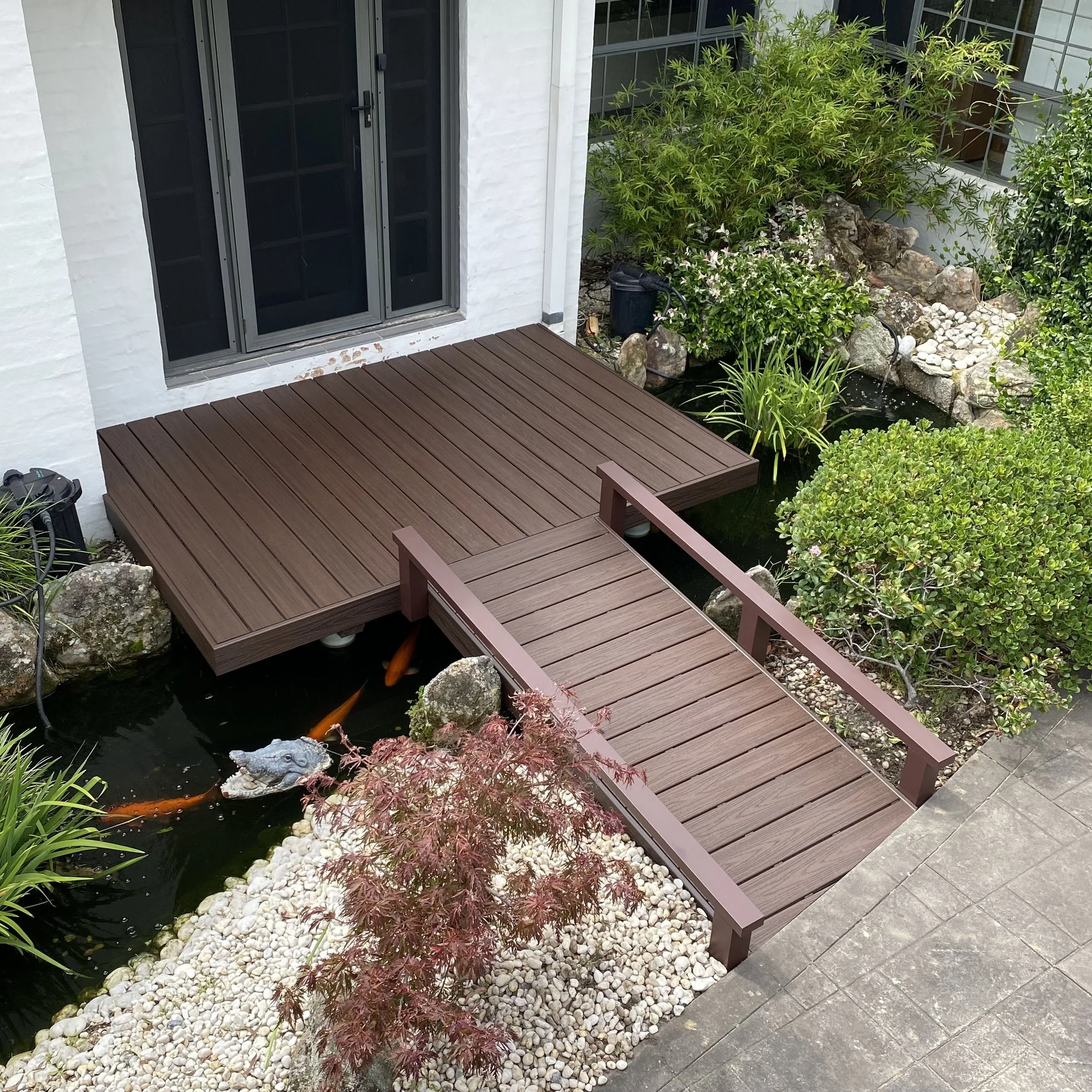 Composite entry deck built over pond with koi fish, surrounded by rocks and plants. Built and designed by Platinum Decks.