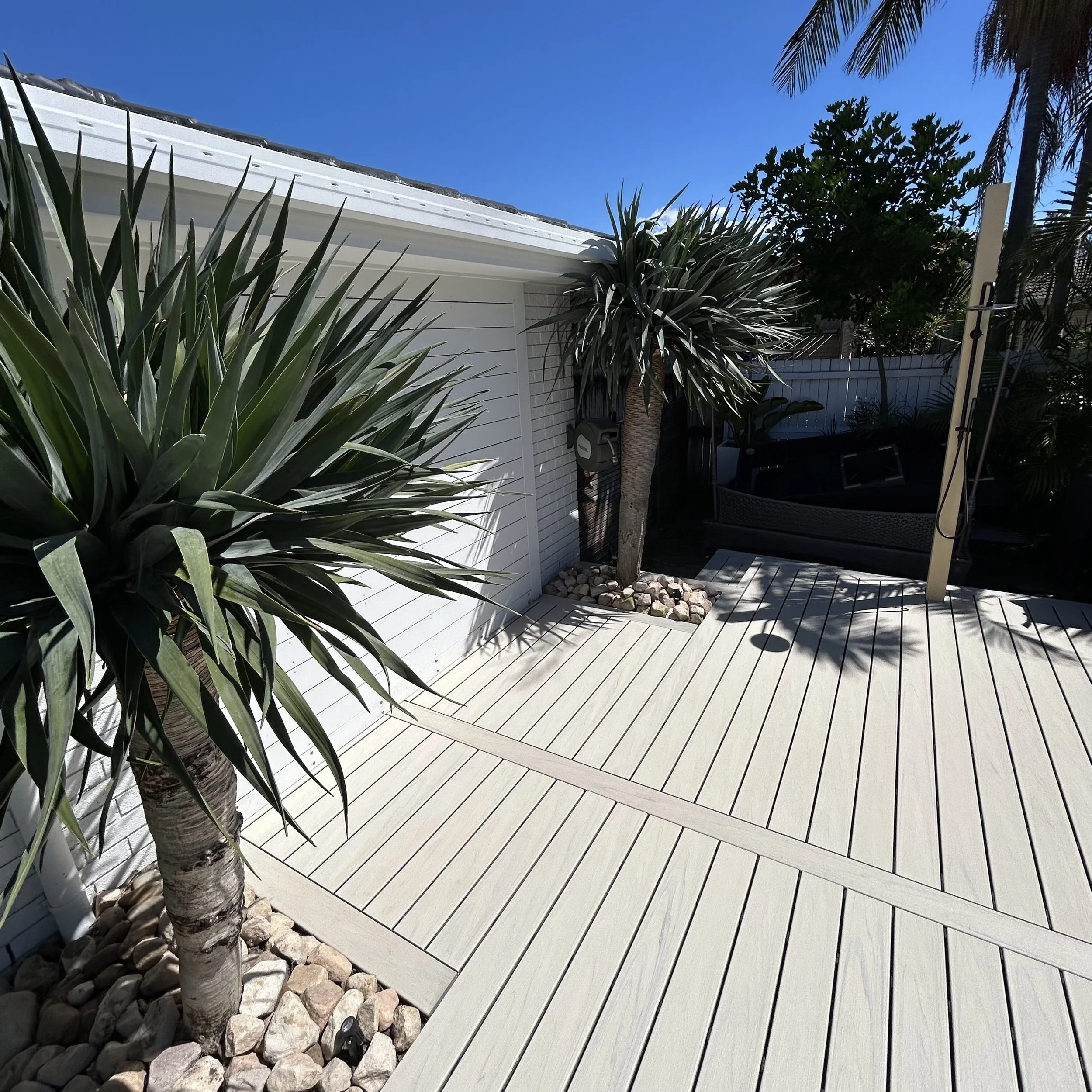 Backyard pool Trex Salt Ash decking with white fencing, palm trees and coastal home backdrop designed by Platinum Decks to blend tropical landscaping with refined outdoor architecture