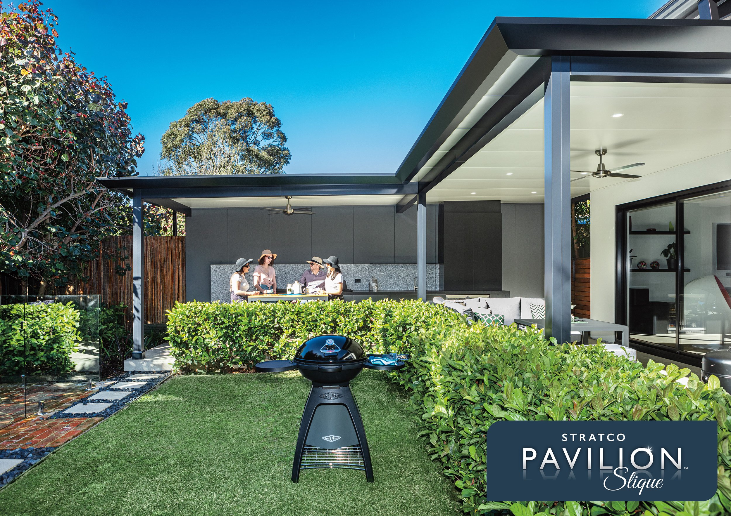 Backyard patio with a covered seating area, four women wearing hats standing and talking, a barbecue grill in the foreground, lush green plants and trees, and a modern house with large windows. Platinum Decks authorised installer.