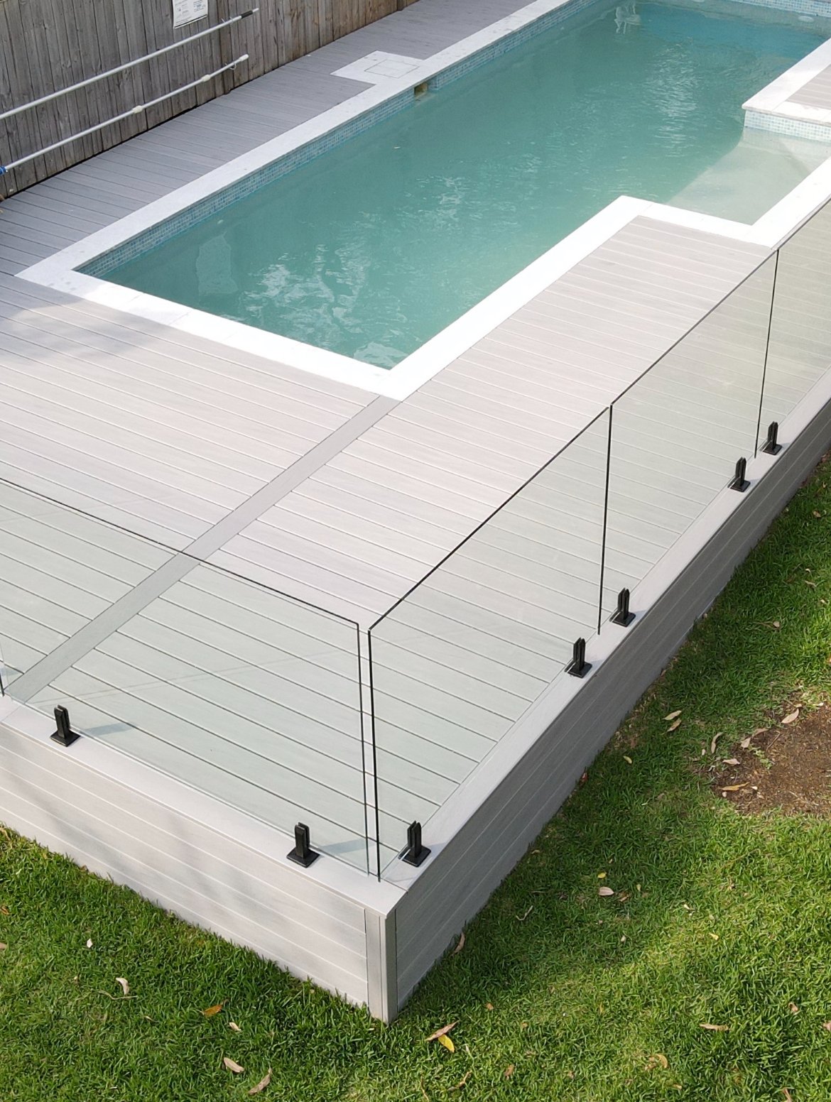 Trex Salt Ash Composite deck surrounding a modern coastal pool with clear glass balustrade, light blue water and green lawn, built by Platinum Decks on the Central Coast.