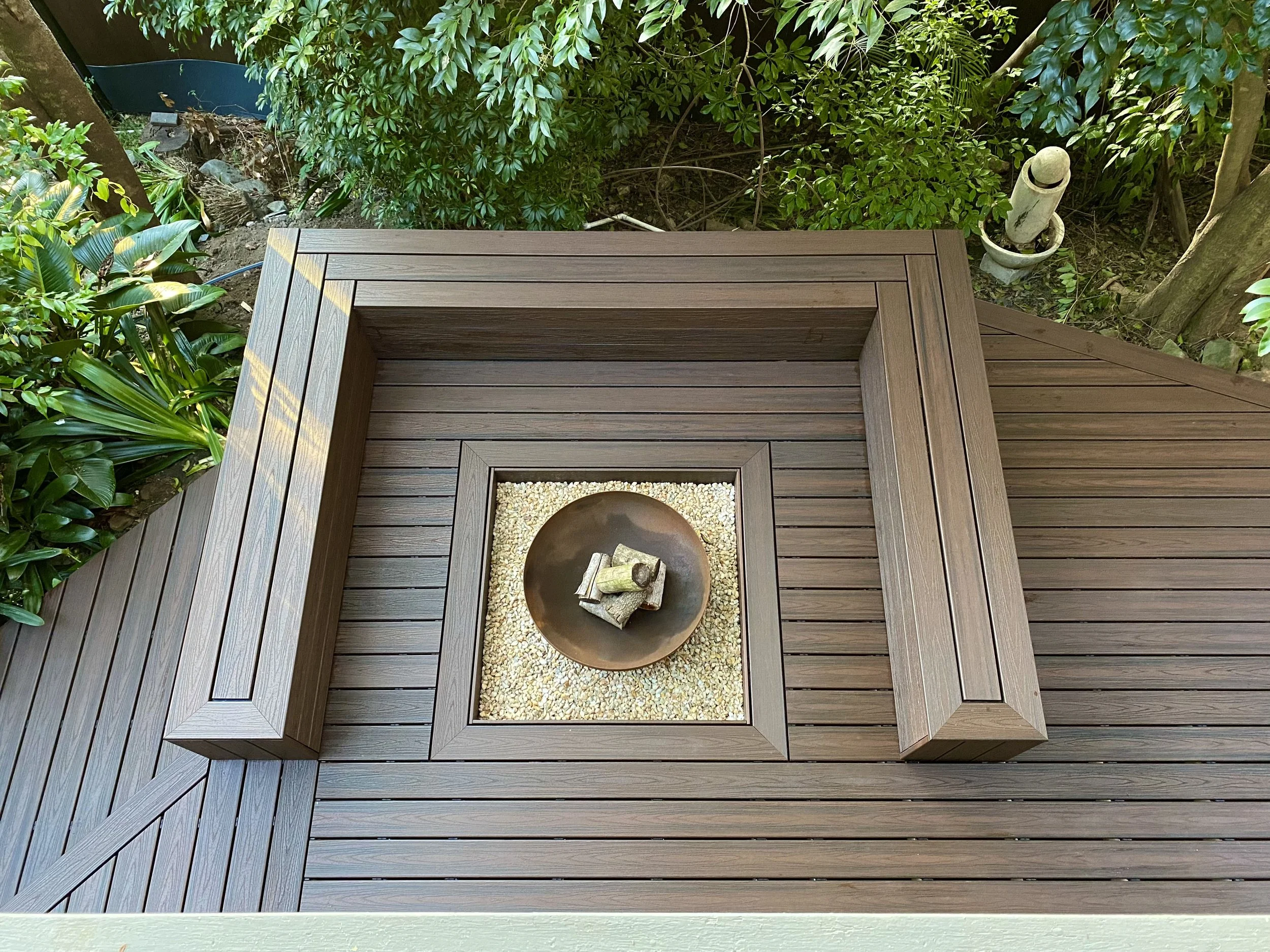 Ariel view of composite fire pit and seating outdoor area adjoining to a composite deck surrounded by green shrubs. Design, installed and built by Platinum Decks.