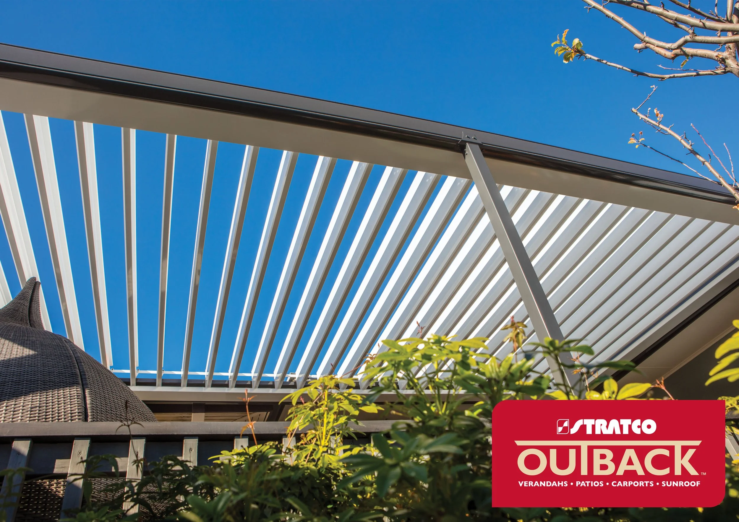 View of a white slatted pergola against a clear blue sky, with some greenery in the foreground, and a red Straco Outback sign in the bottom right corner. Platinum Decks authorised installer.