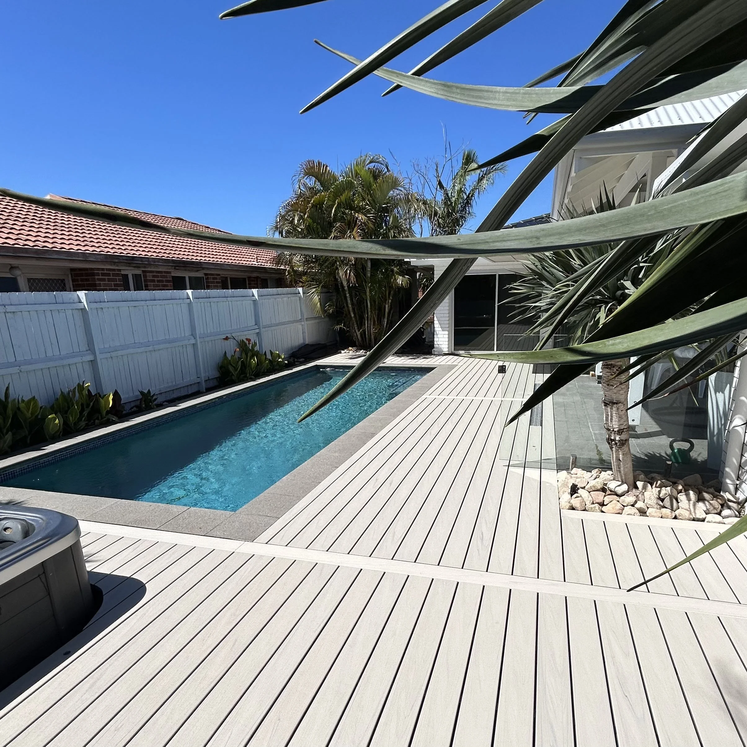 Backyard pool Trex Salt Ash decking with white fencing, palm trees and coastal home backdrop designed by Platinum Decks to blend tropical landscaping with refined outdoor architecture
