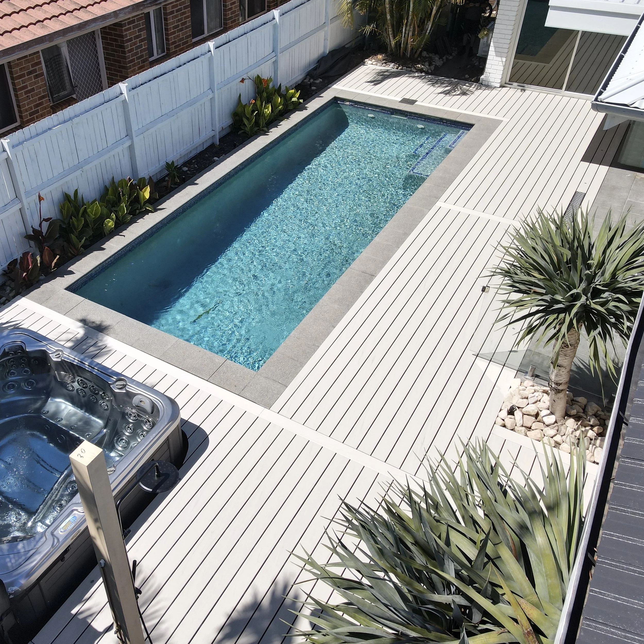 Backyard pool Trex Salt Ash decking with white fencing, palm trees and coastal home backdrop designed by Platinum Decks to blend tropical landscaping with refined outdoor architecture