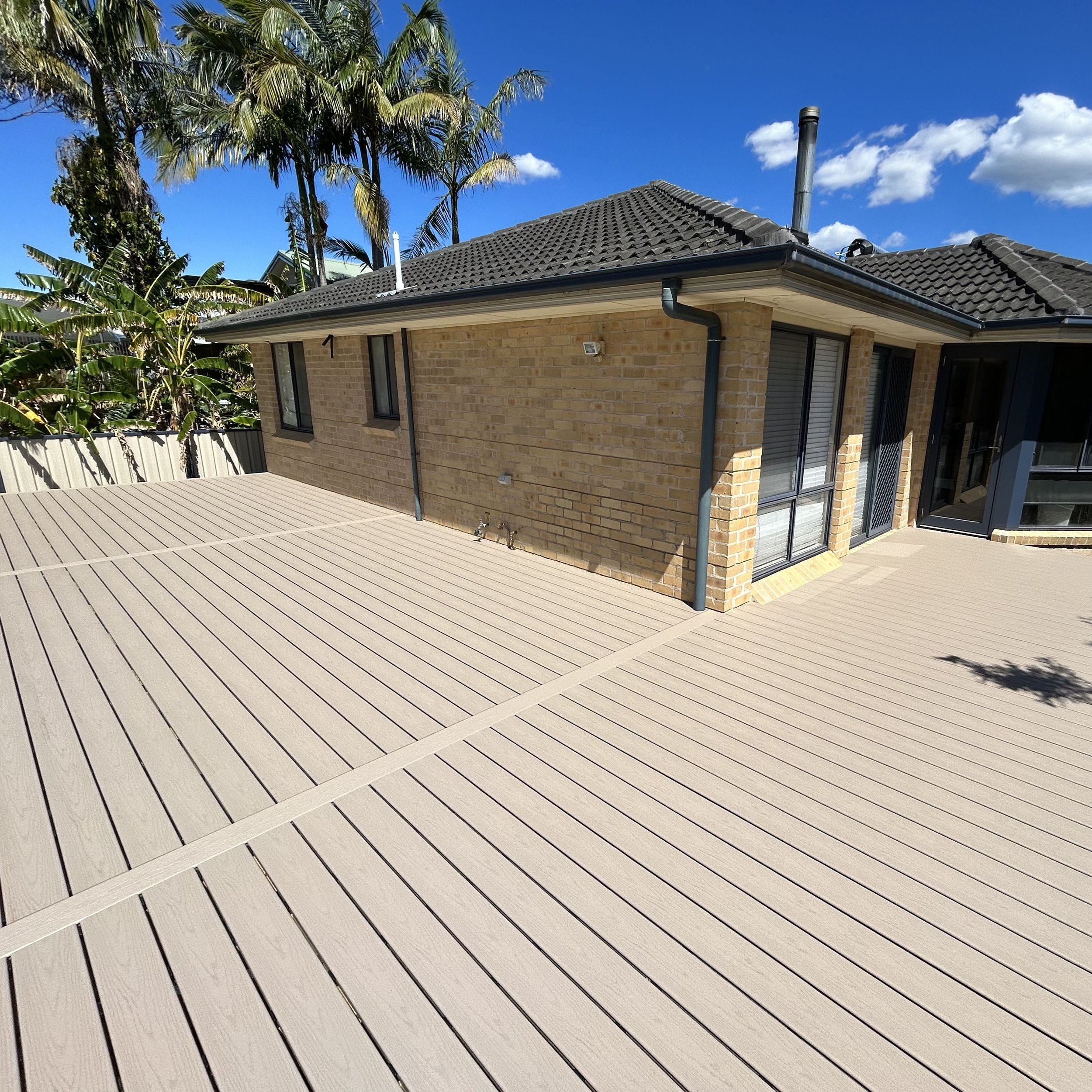 Coastal‑style home framed by palms and outdoor living zones enhanced by Platinum Decks to complement premium Central Coast architecture