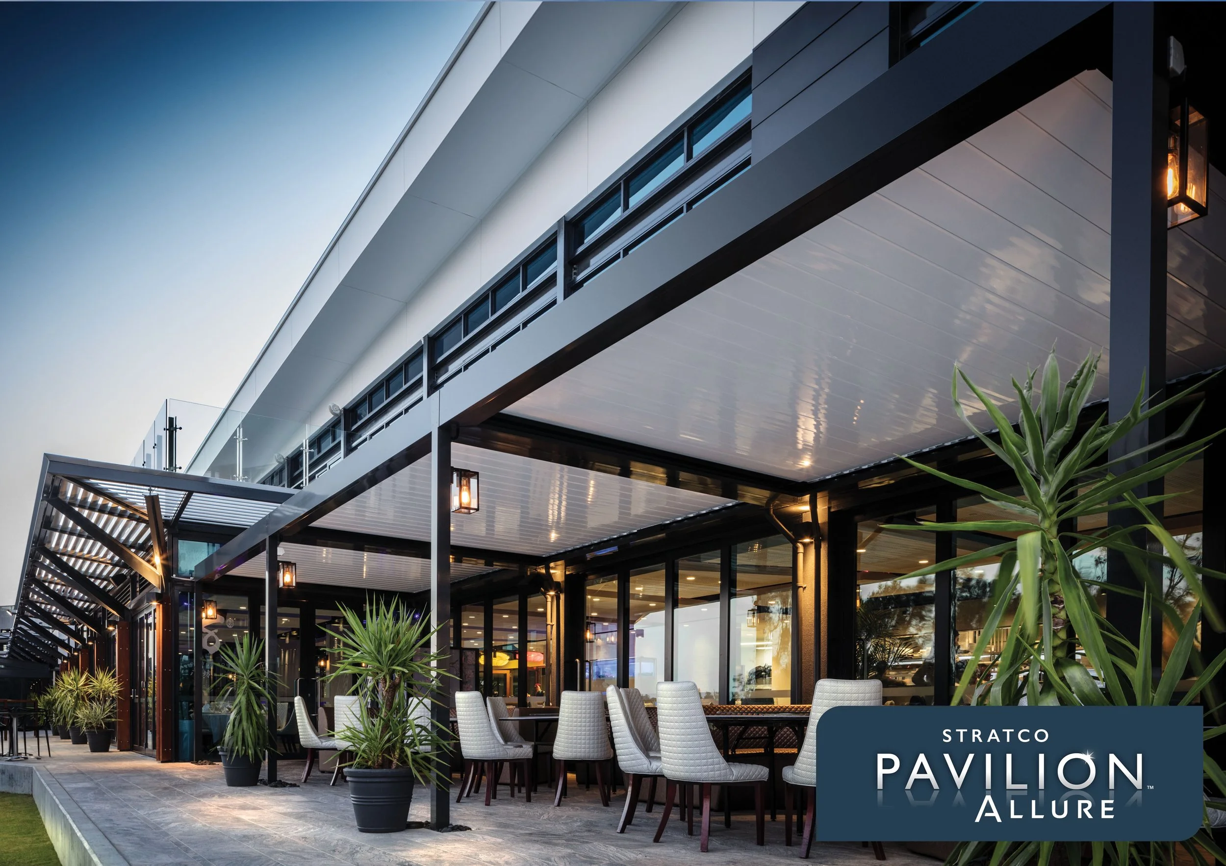 Modern outdoor pavilion with glass walls, potted plants, and seating area, illuminated by warm lighting at dusk. Platinum Decks authorised installer.