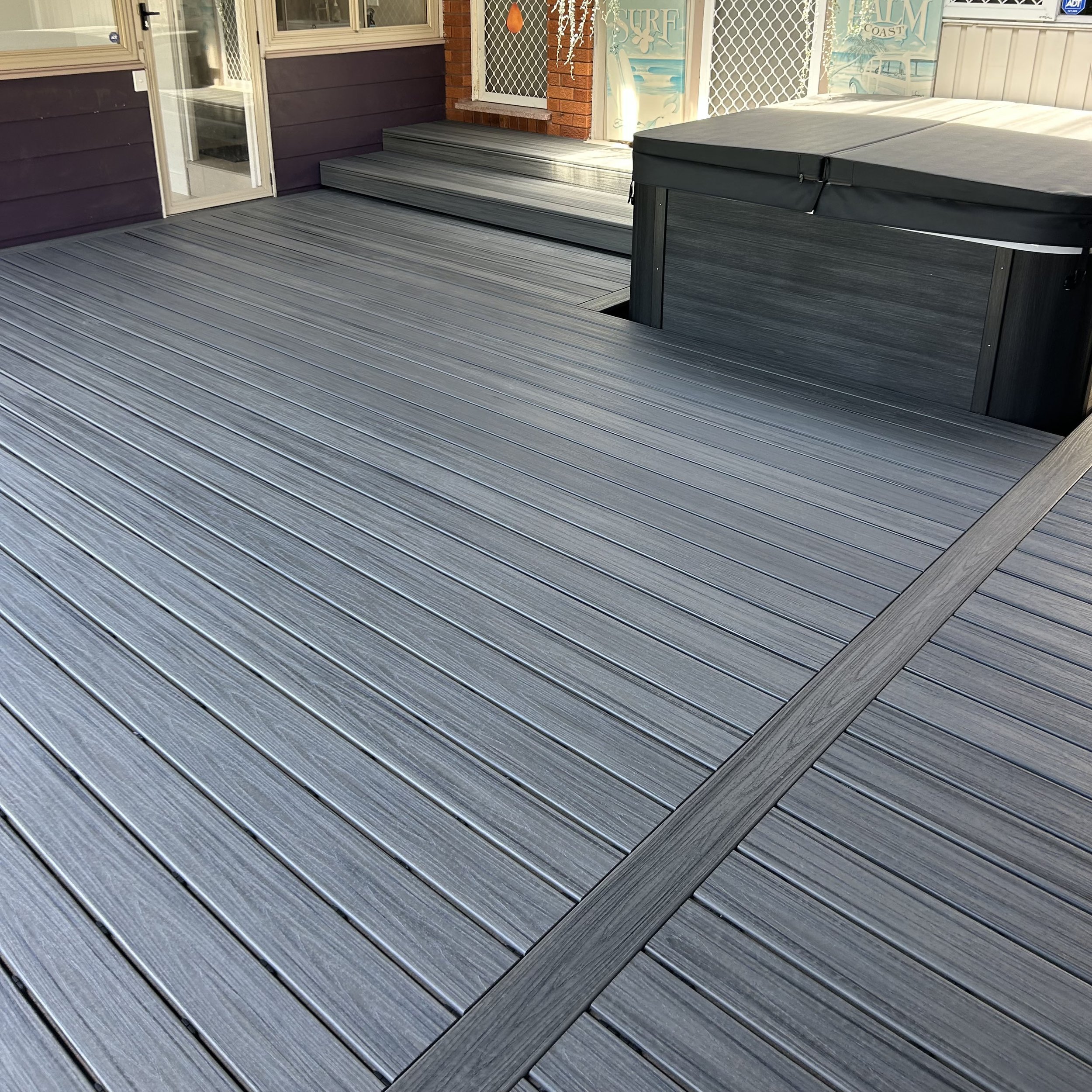 A modern composite deck with steps leading up to a door, and a spa area. Stylishly built by Platinum Decks.