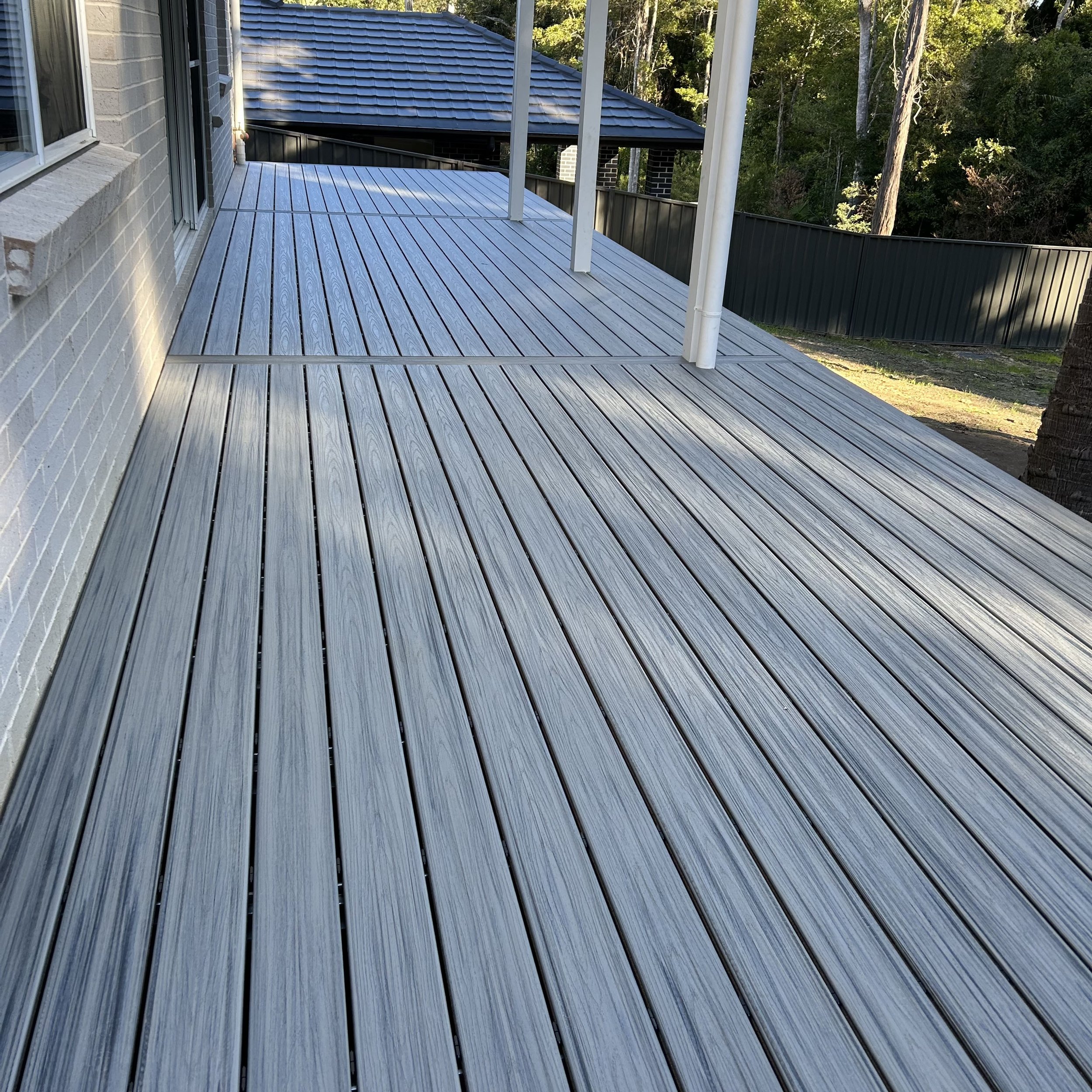 View of a new composite deck attached to a house, with a metal railing and forest in the background.