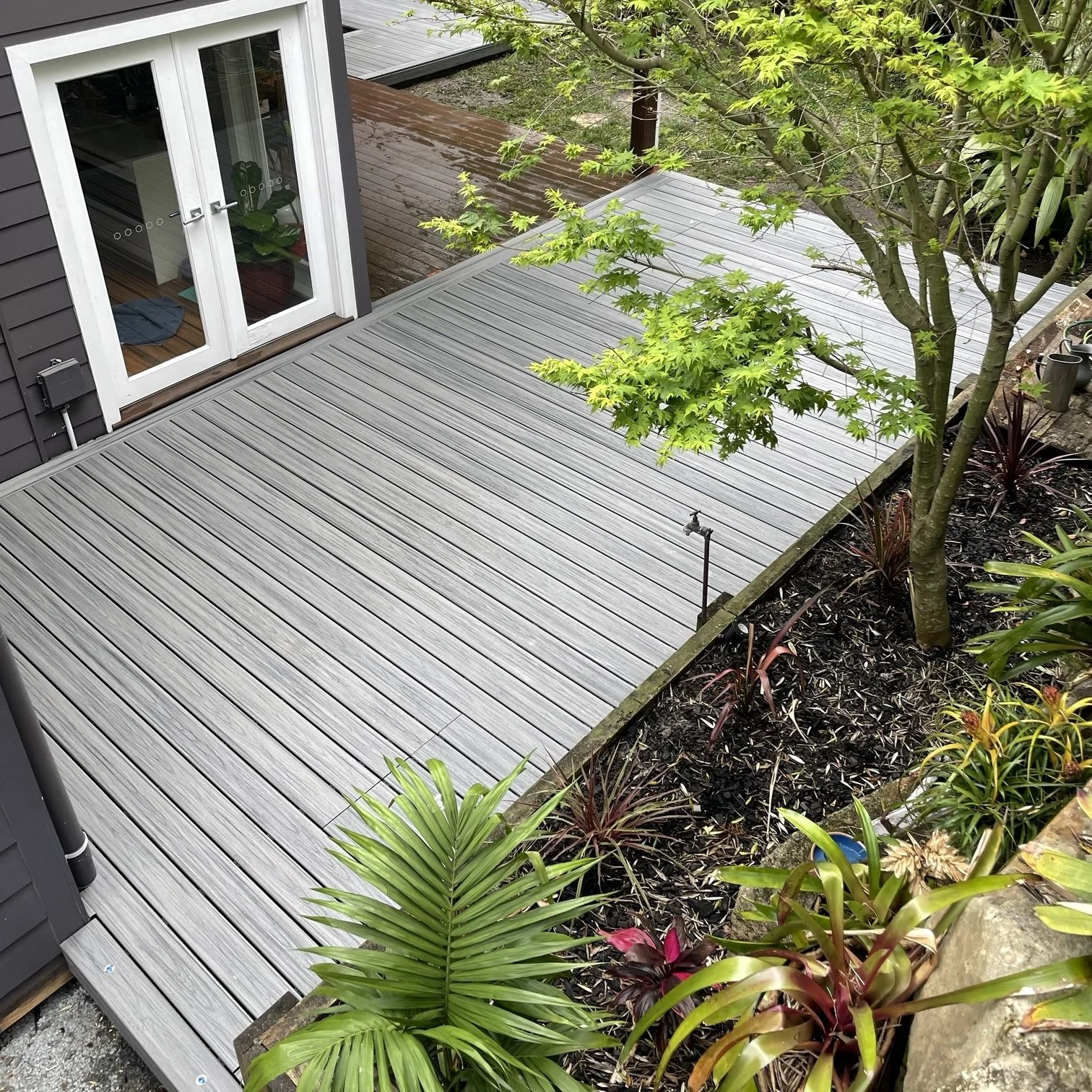 Trex composite deck in Island Mist beside landscaped garden feature crafted by Platinum Decks to blend luxury outdoor living with natural greenery