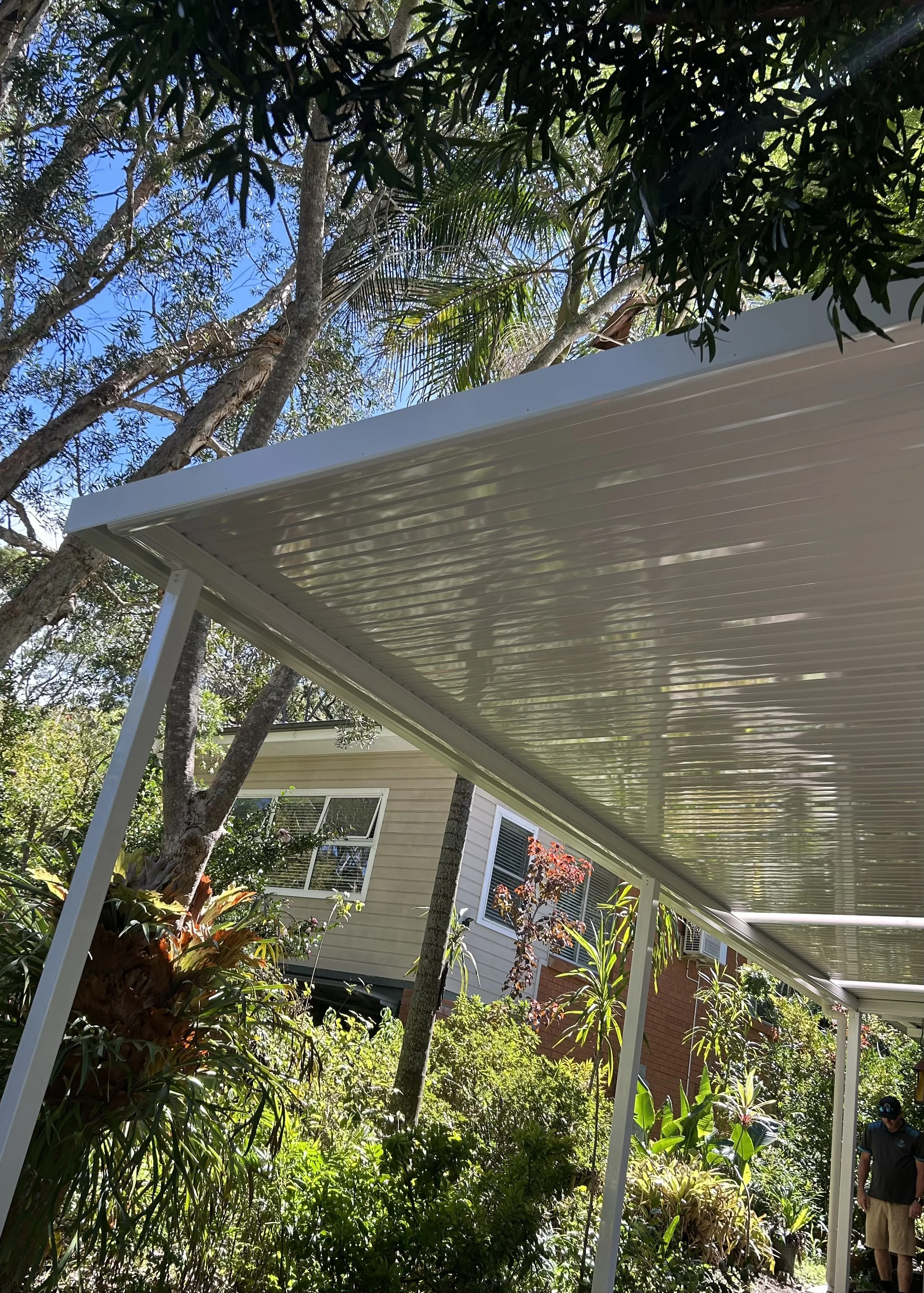 Stratco carport extending over lush backyard greenery enhanced by Platinum Decks to create a relaxed, coastal‑ready outdoor living zone