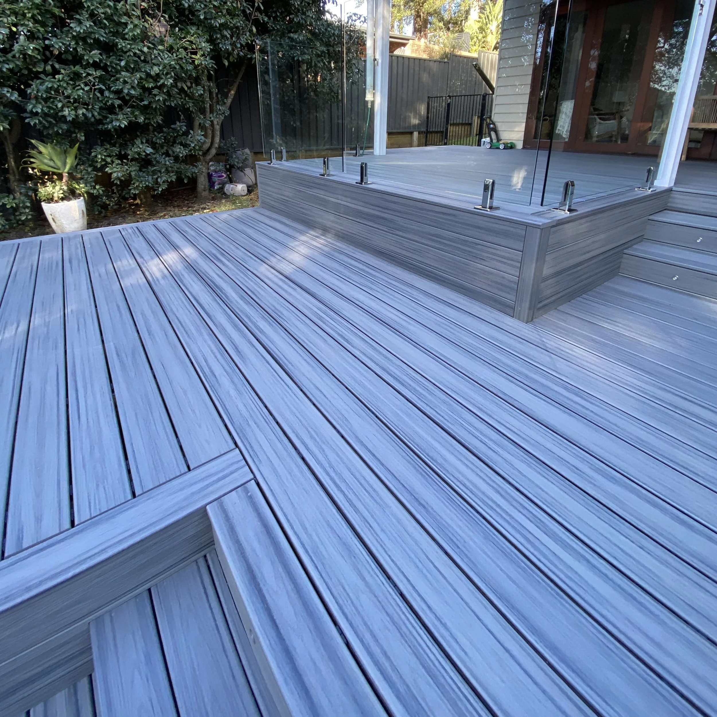 Backyard patio with wooden decking, glass railing, plants, and a small toy in the corner.